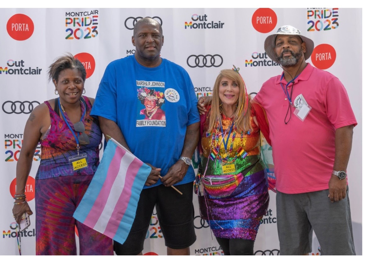 Four people standing together at an event, with a backdrop displaying logos and text, smiling for the photo.