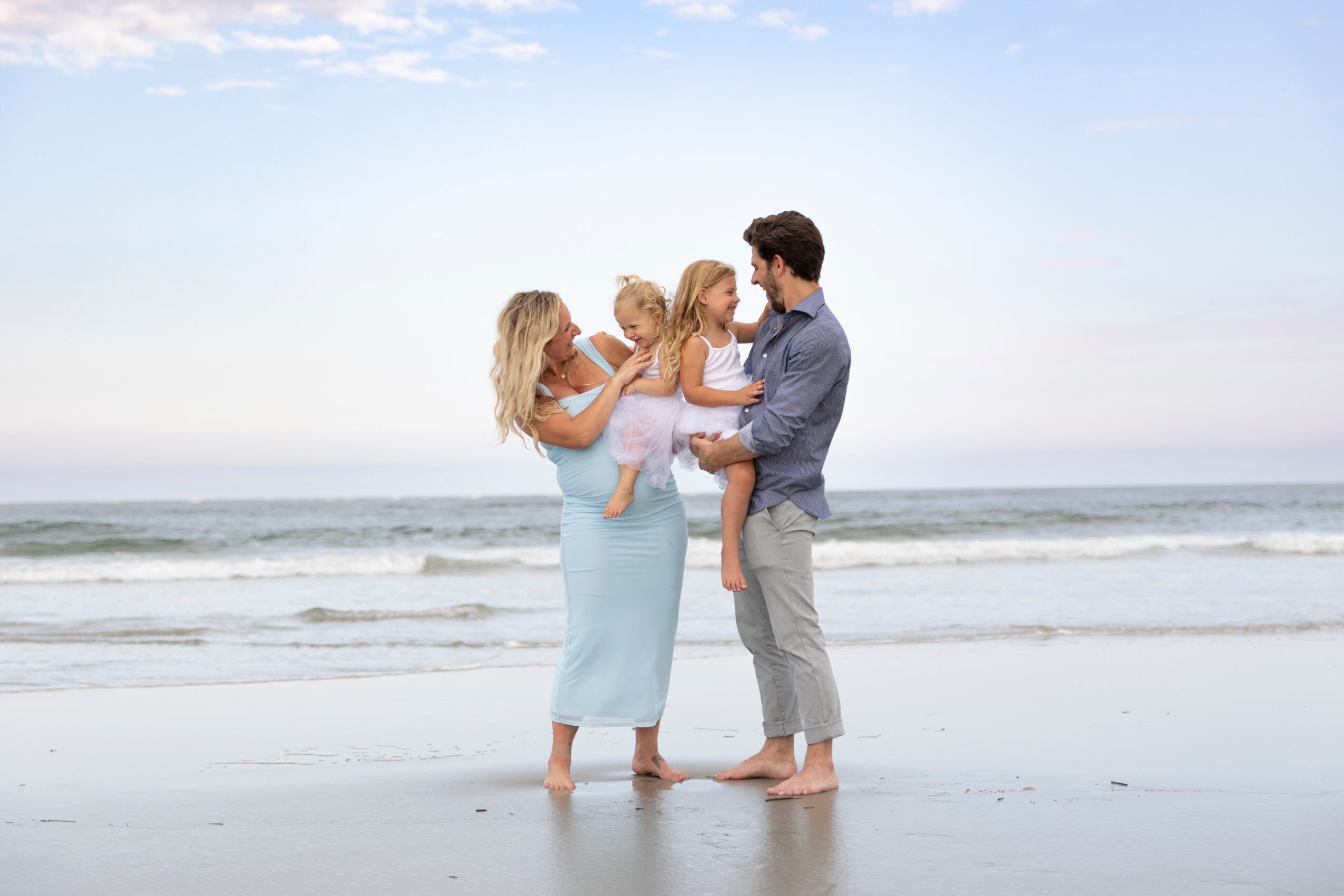 Family of four on the beach, with two children and two adults, standing near the shoreline with ocean waves in the background.