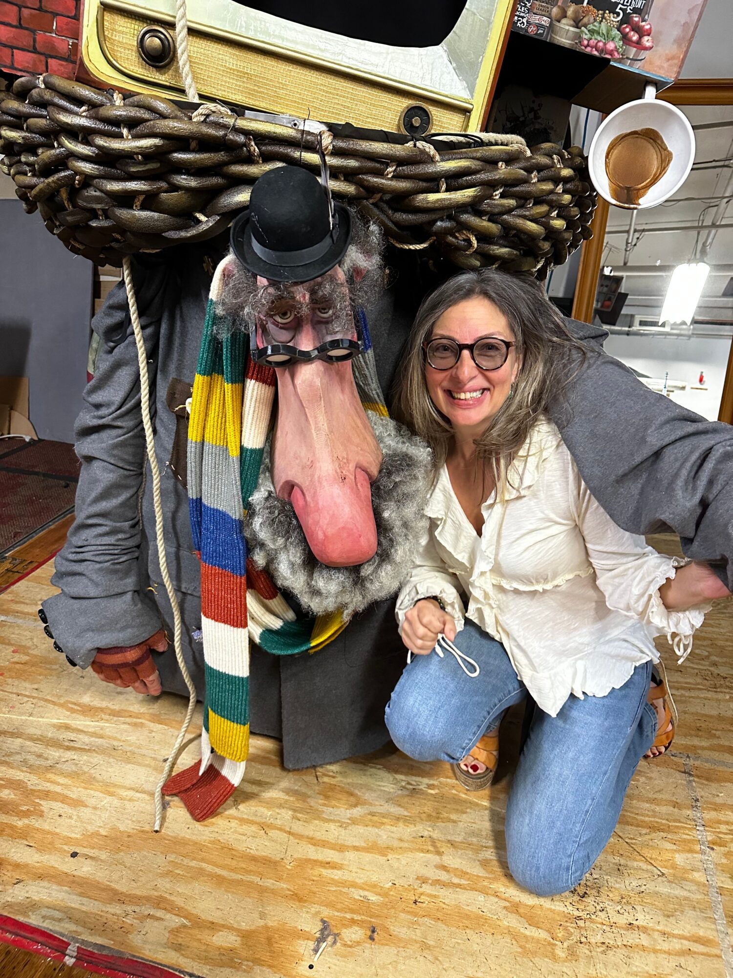 Person with glasses and a hat holding a dog, sitting on the floor with a woman nearby, in a room with wooden flooring.