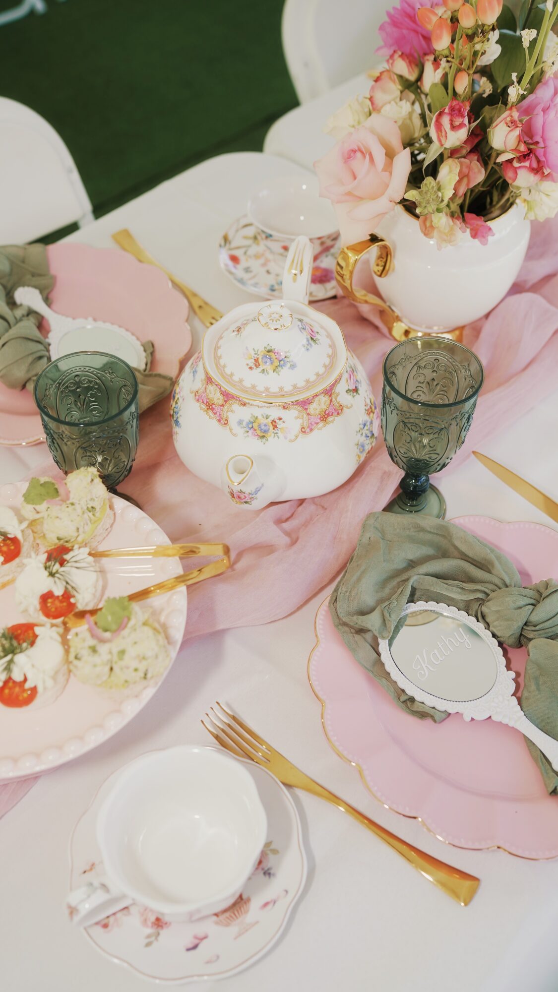 Table setting with floral centerpiece, teapot, cups, plates, and cutlery, decorated in pastel colors.