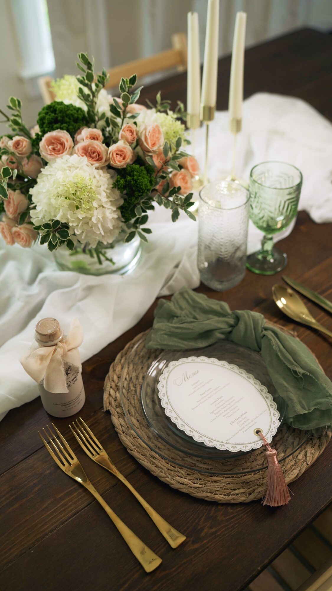 Table setting with floral centerpiece, candles, glassware, and place setting with gold utensils and green napkin.