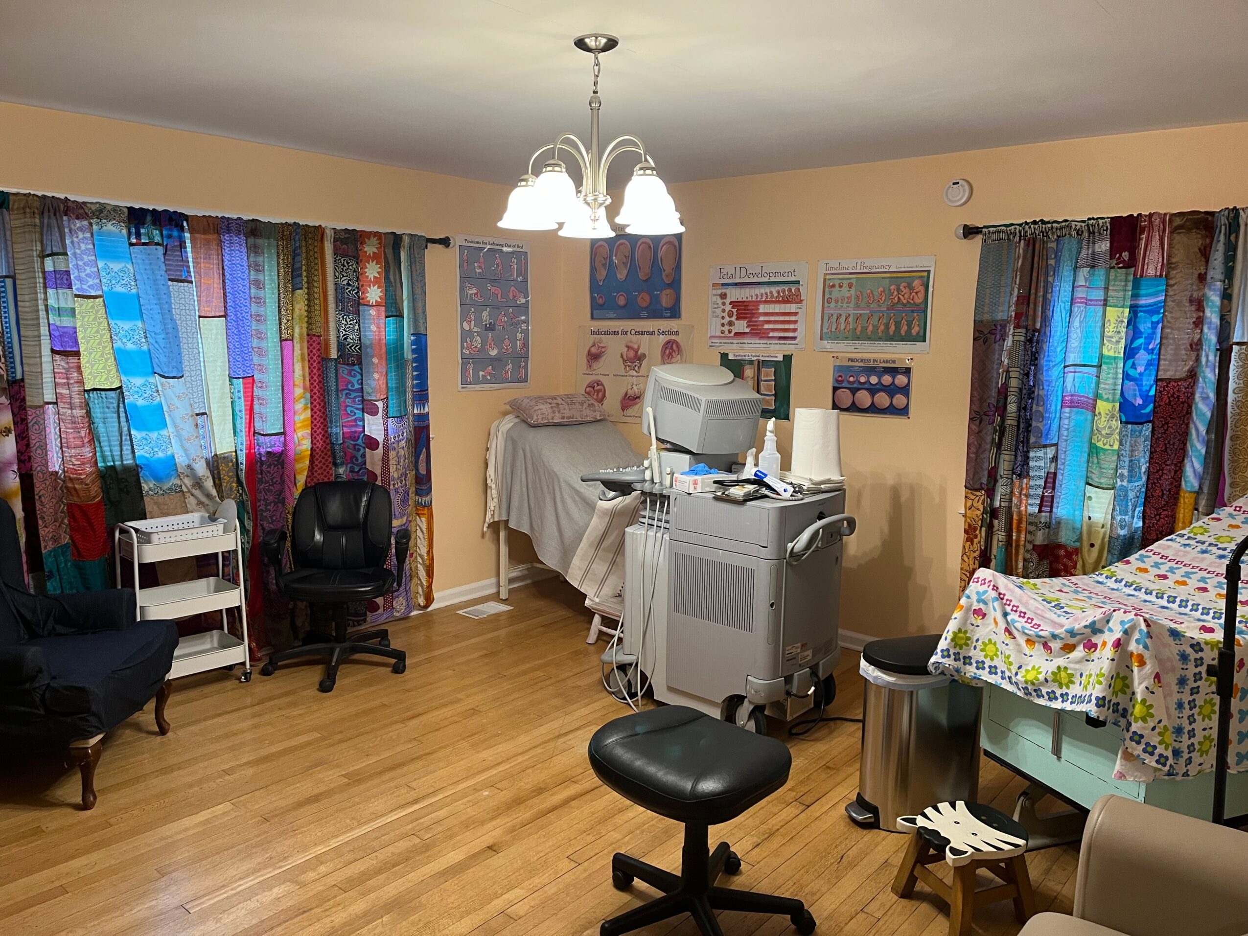 Hospital room with medical equipment, bed, chairs, and colorful curtains, illuminated by a ceiling light fixture.