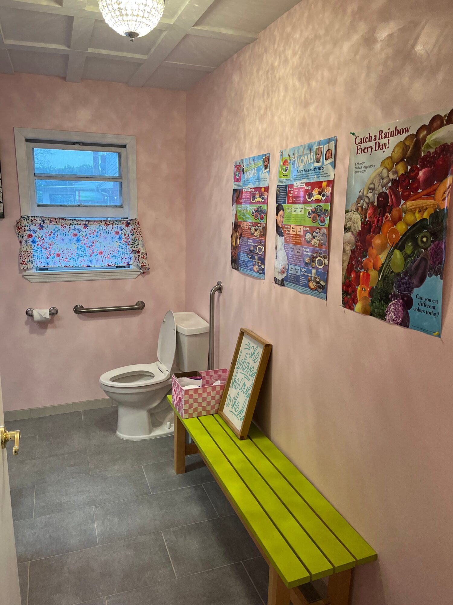Bathroom with pink walls, a window with a colorful curtain, a green cabinet, and a toilet.