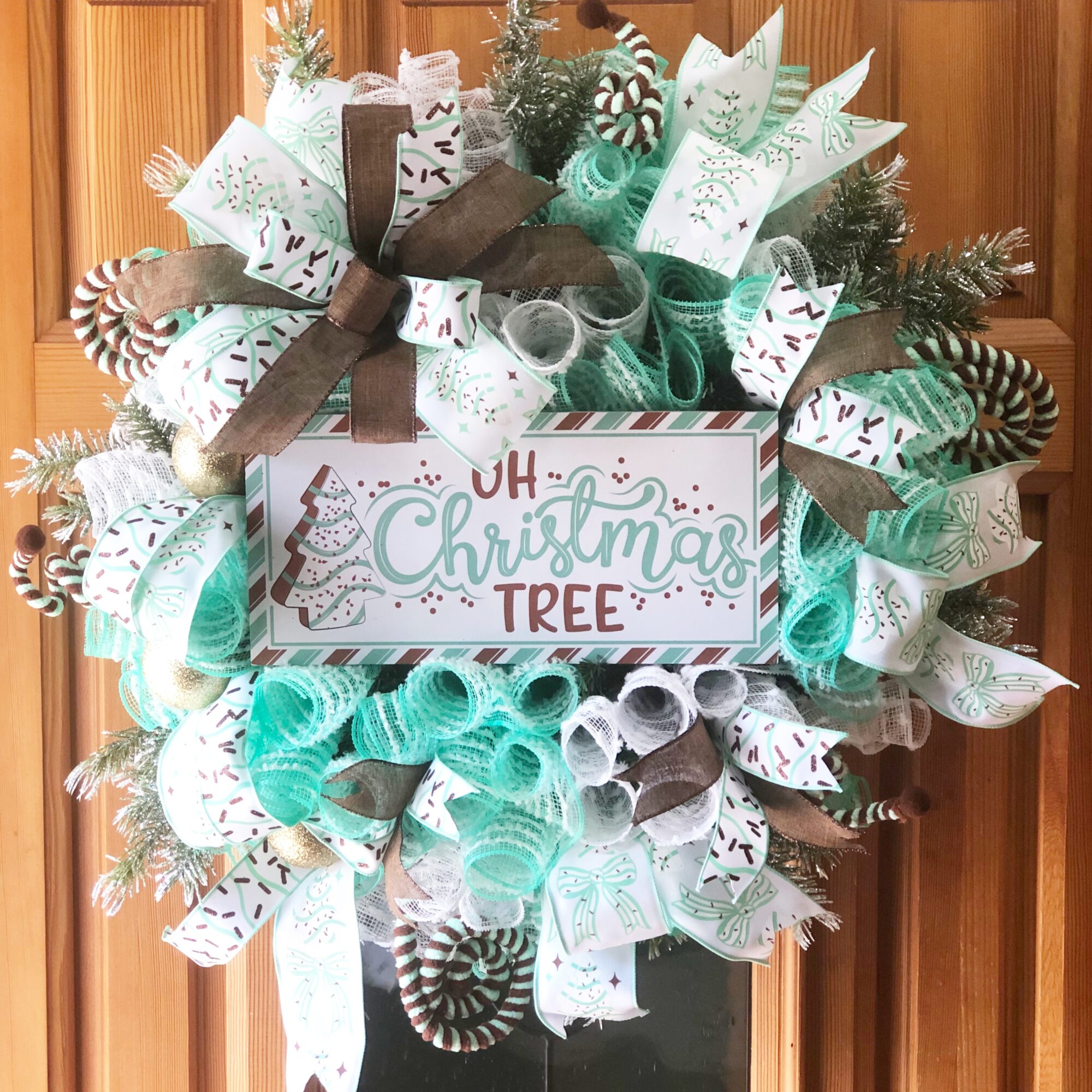 Decorative Christmas wreath with ribbons, pine branches, and a sign reading 'Oh Christmas Tree'.