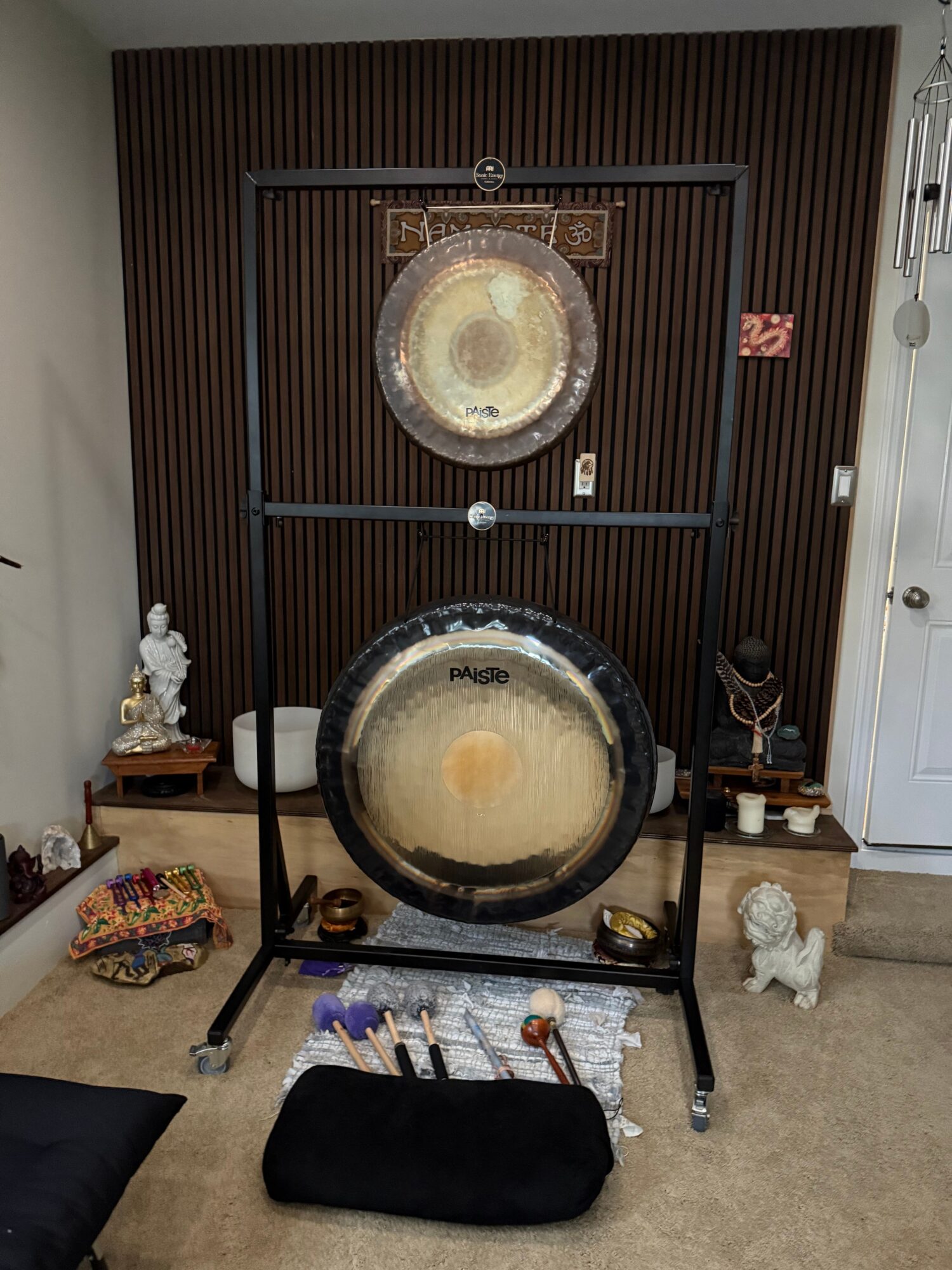 Two large gongs on stands in a room with wooden wall paneling, a black cushion, and various decorative items.