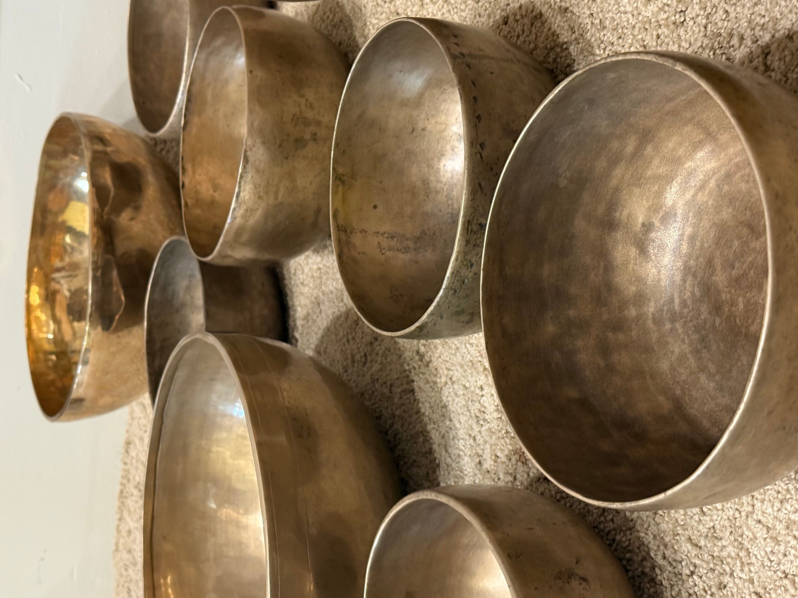 Multiple metallic singing bowls of various sizes arranged on a surface, some overlapping, with a textured background.