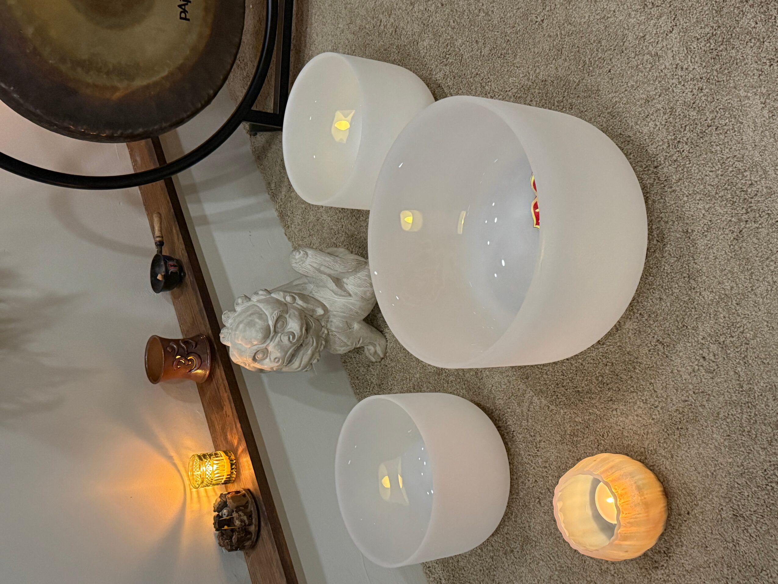 Three white ceramic bowls and a small pumpkin-shaped candle holder on a gray surface, with a decorative lion sculpture and a lamp in the background.