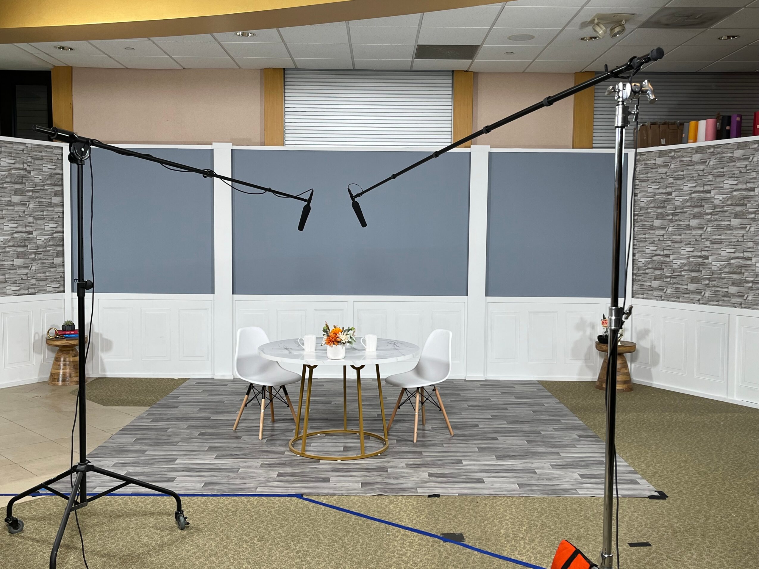 Set up for a video or photo shoot with a table and four chairs in a room, with lighting equipment visible.