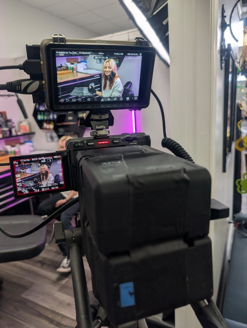 Camera capturing a woman sitting in a vehicle, with a display screen showing her image, in an indoor setting.