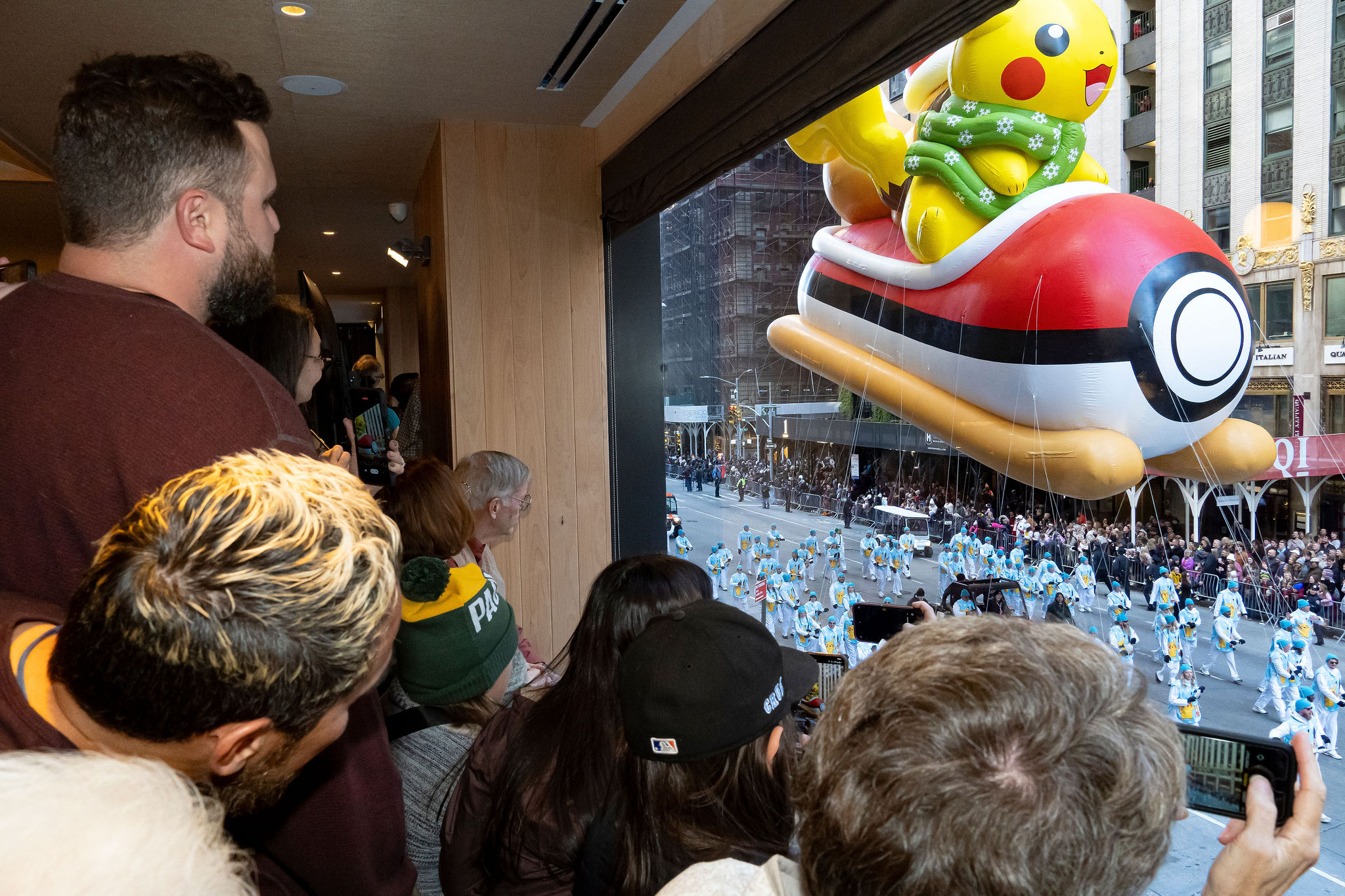 People looking at a large Pokémon-themed float in a city street, with buildings and a parade in the background.
