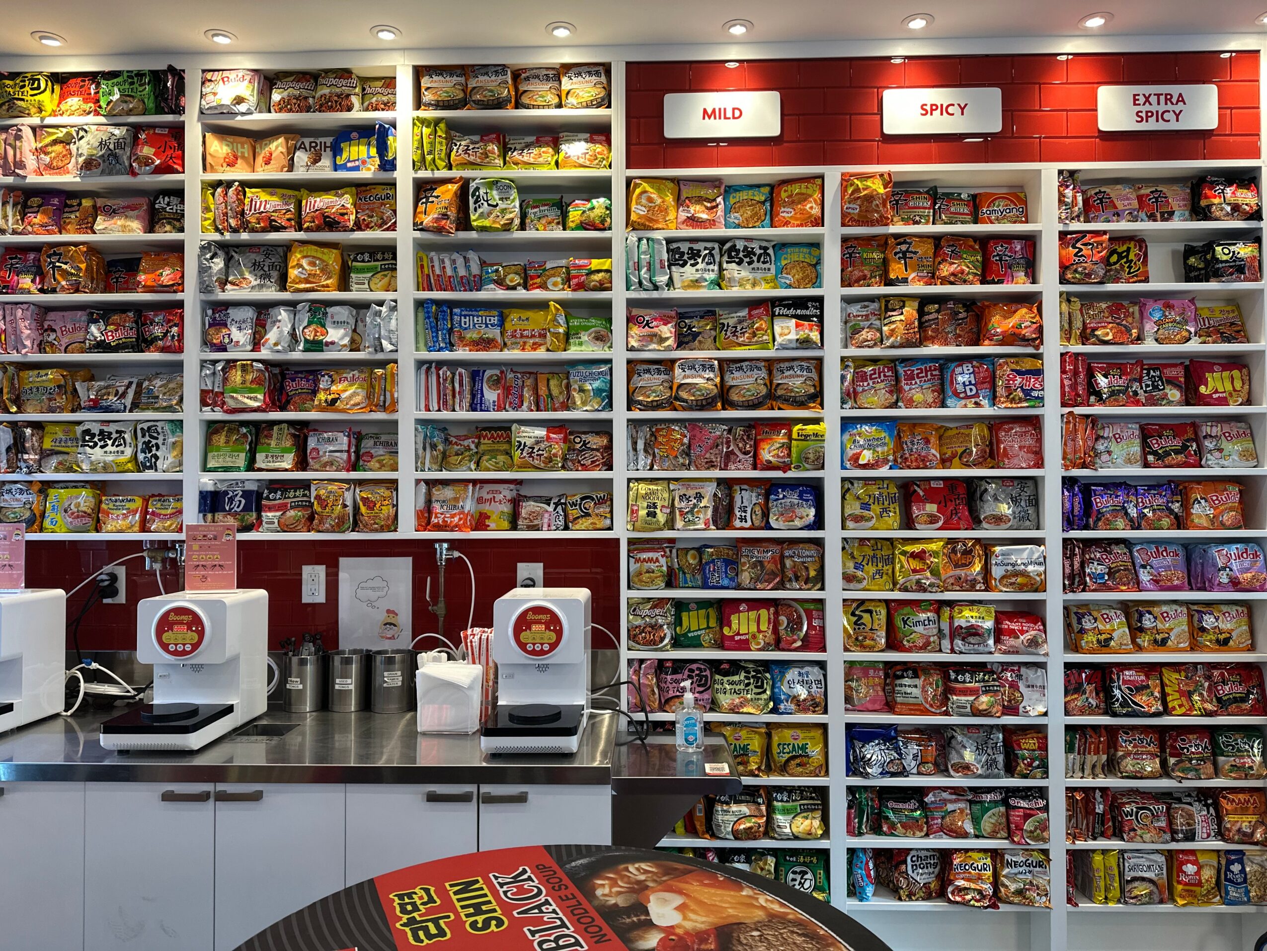 Snack shelves filled with various colorful snack bags and chips, with red and white signs above, in a store aisle.