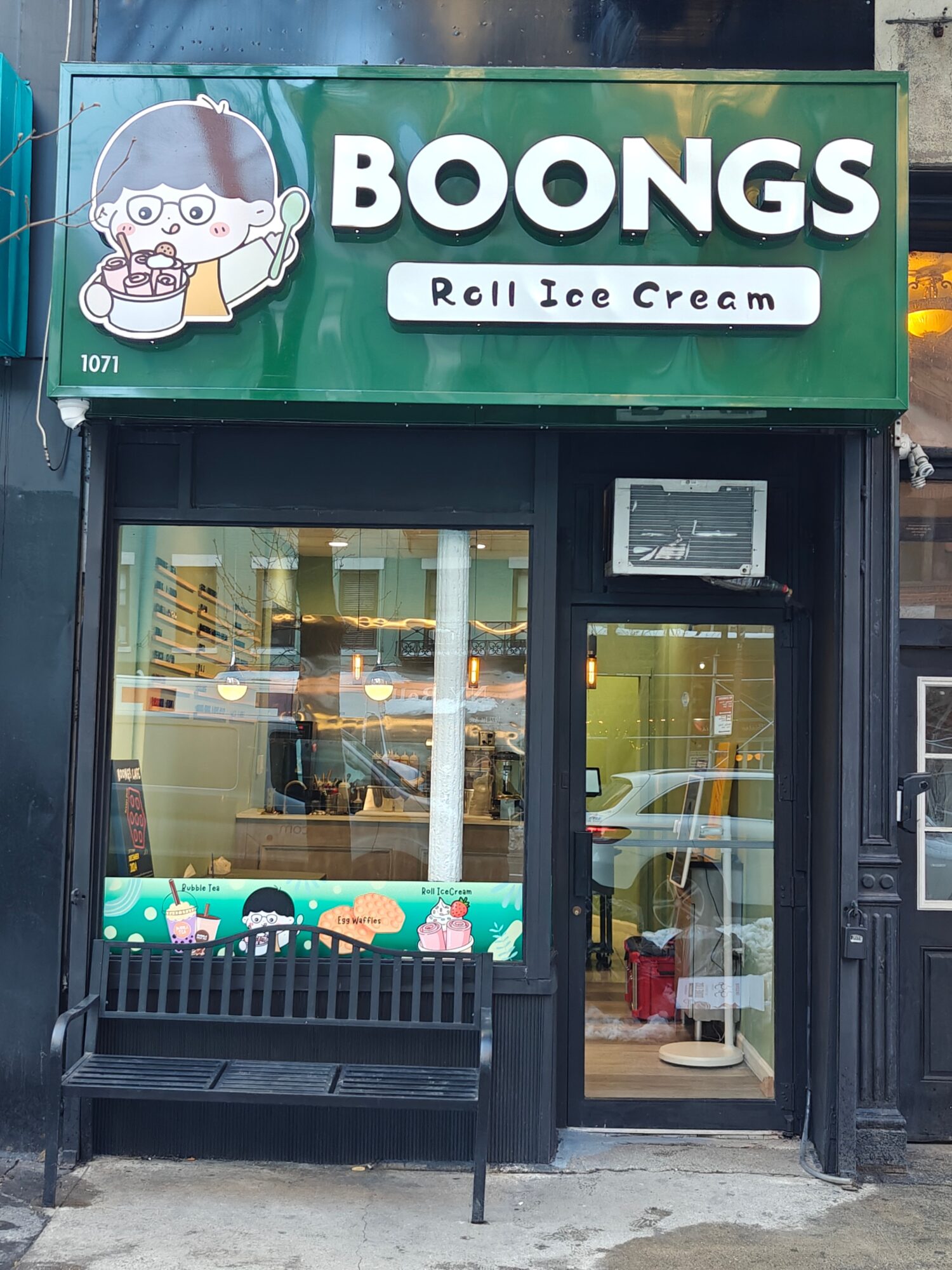 Storefront with a sign reading 'BOONGS Roll Ice Cream' and a cartoon character holding ice cream, black door and window, bench outside.