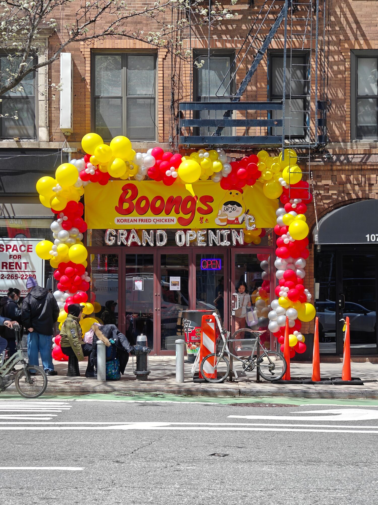 Store entrance decorated with yellow, red, and white balloons, with a sign reading 'Booma's' and a crowd outside.