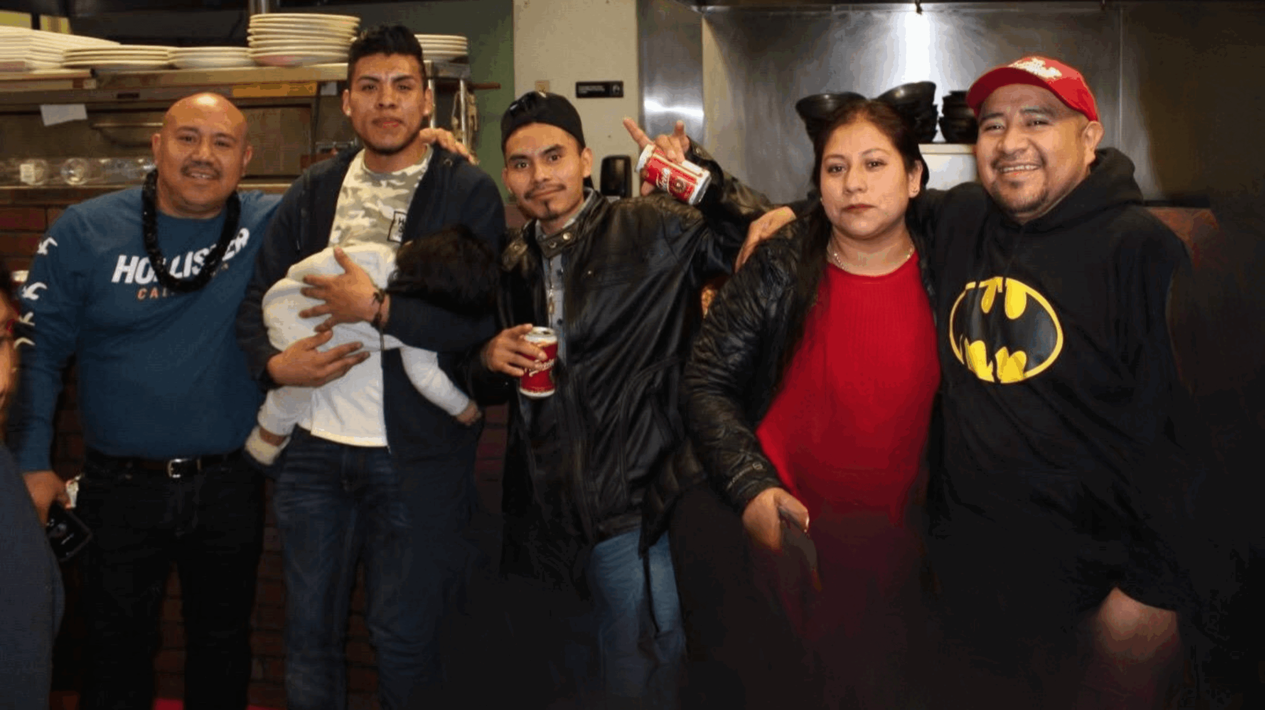 Group of five people standing together indoors, some holding drinks, smiling, and wearing casual clothing.