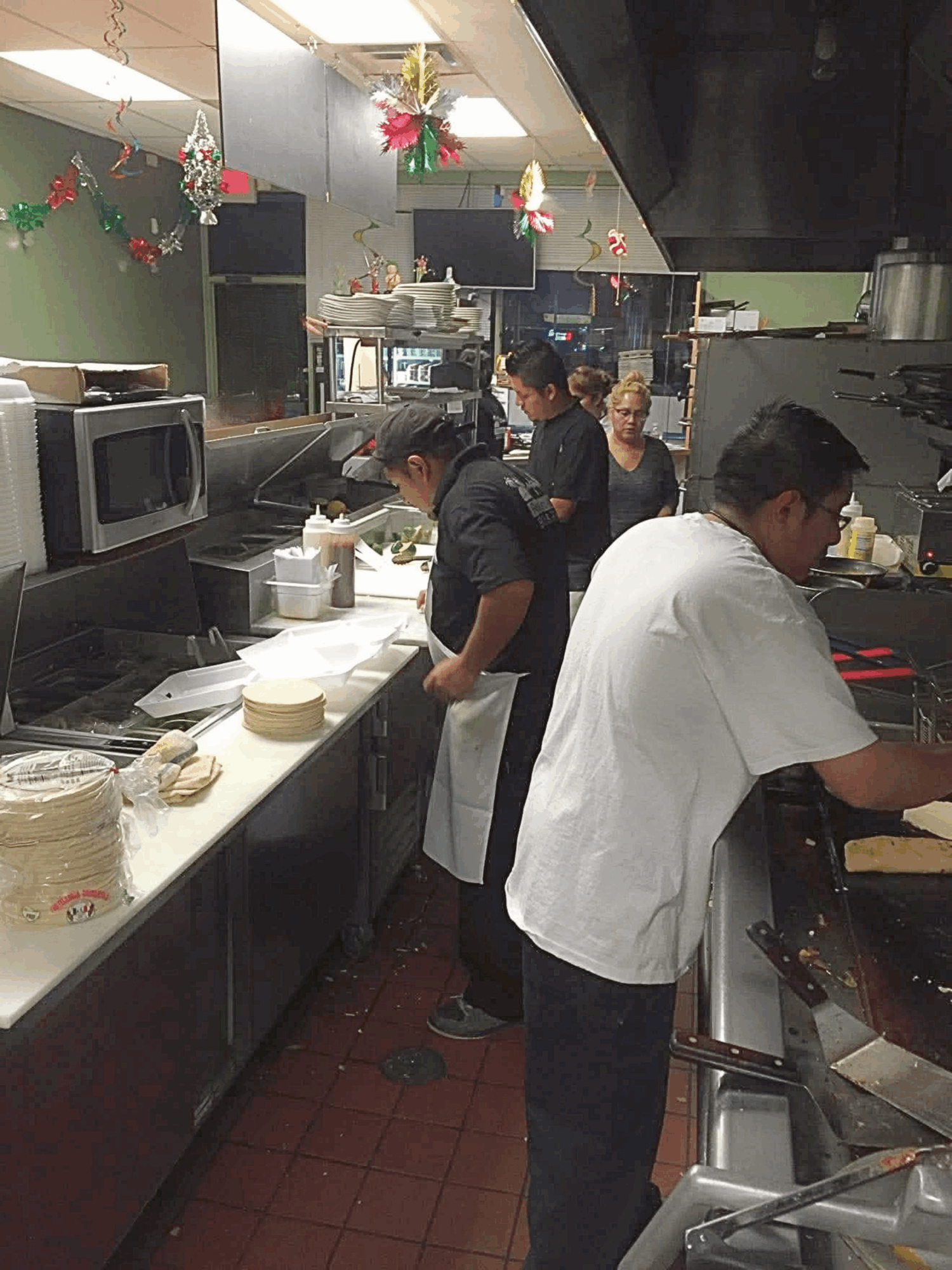 Kitchen with four people preparing food, decorated with hanging ornaments, stainless steel counters, and appliances.