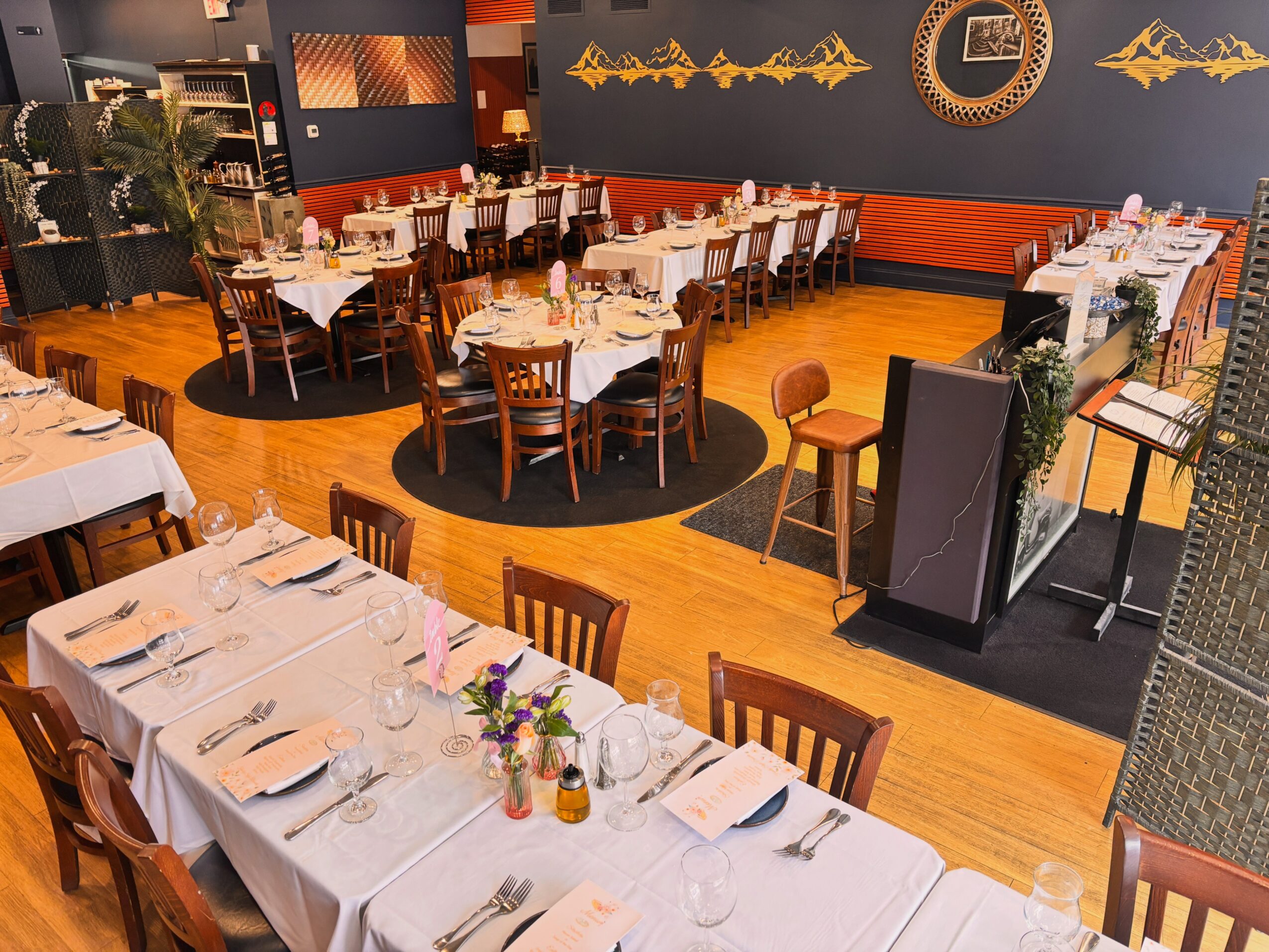Elegant restaurant with long tables, white tablecloths, and chairs, decorated for a formal event, with warm lighting and wooden floors.