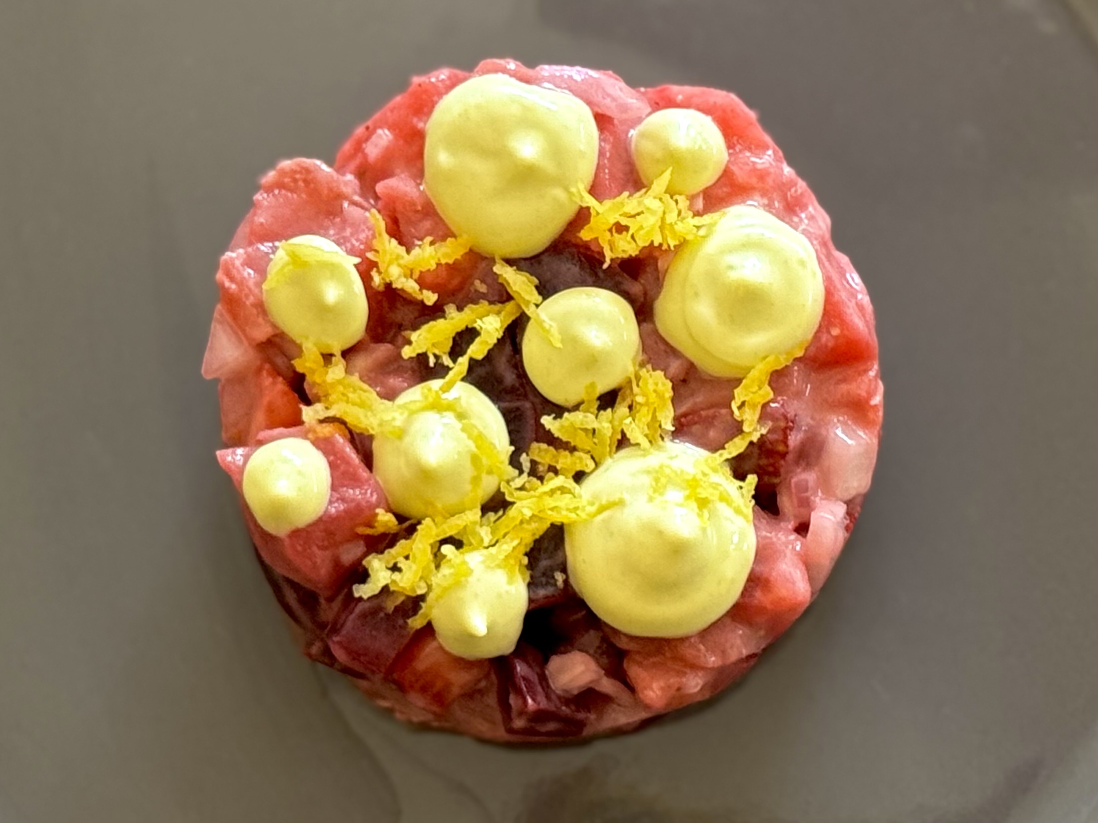Round dessert topped with yellow cream and yellow fruit-like decorations, on a dark surface.