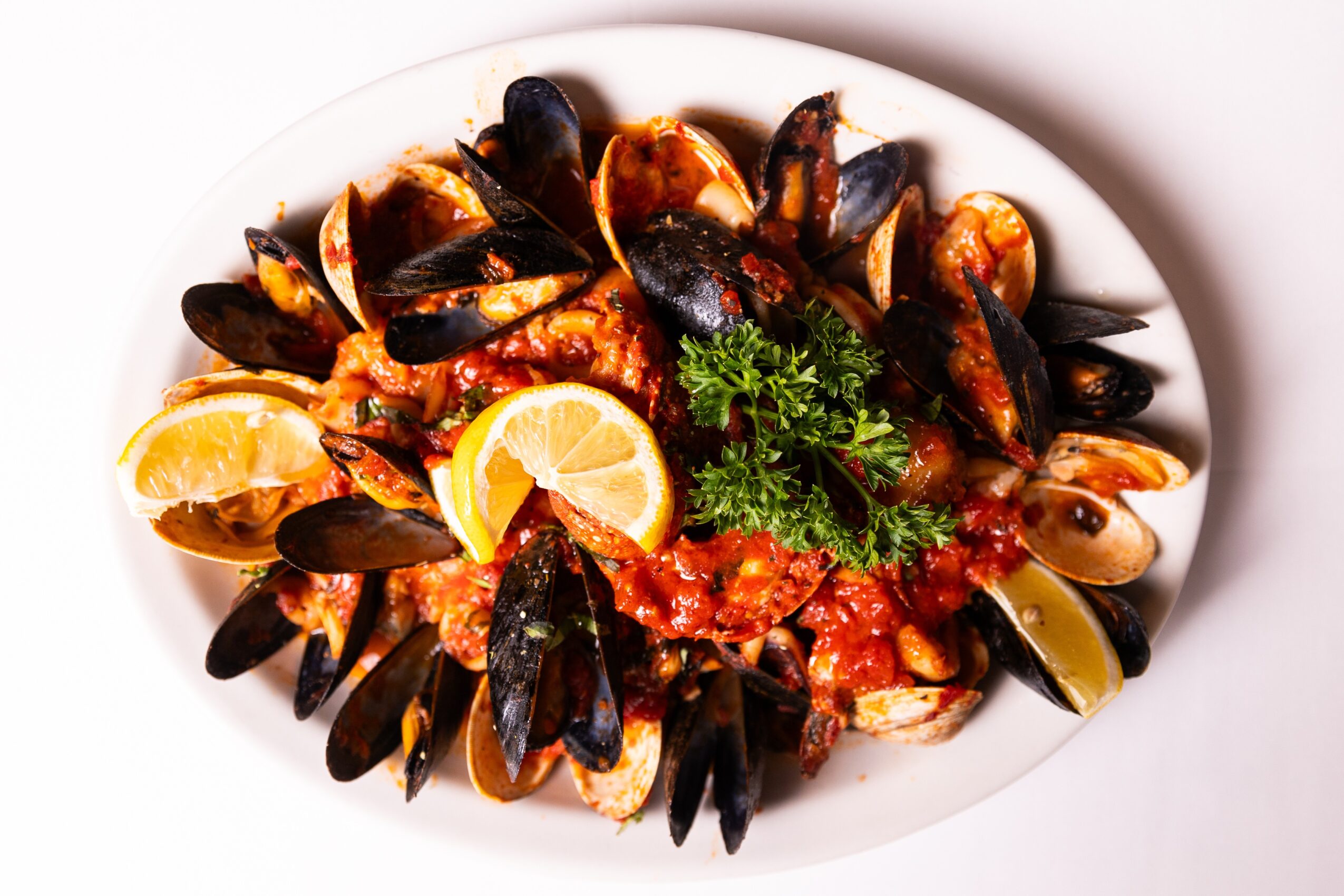 Seafood dish with mussels, lemon wedges, and parsley on a white plate.