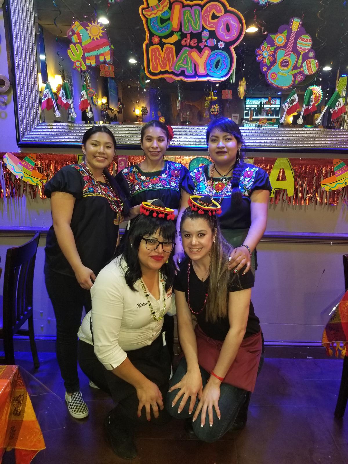 Five women pose in front of colorful decorations and a sign that says