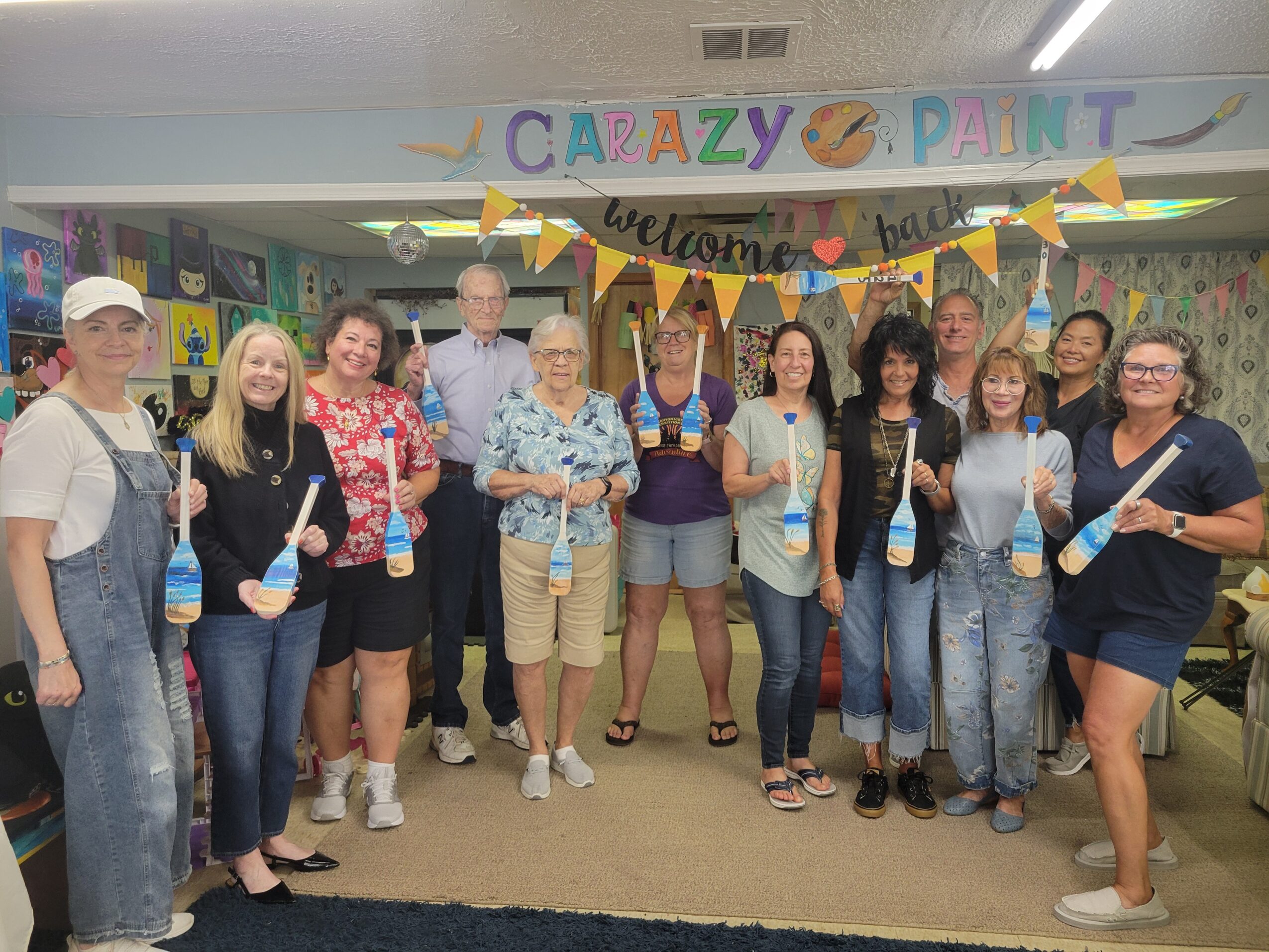 Group of people holding paint bottles in a decorated room with a banner that says