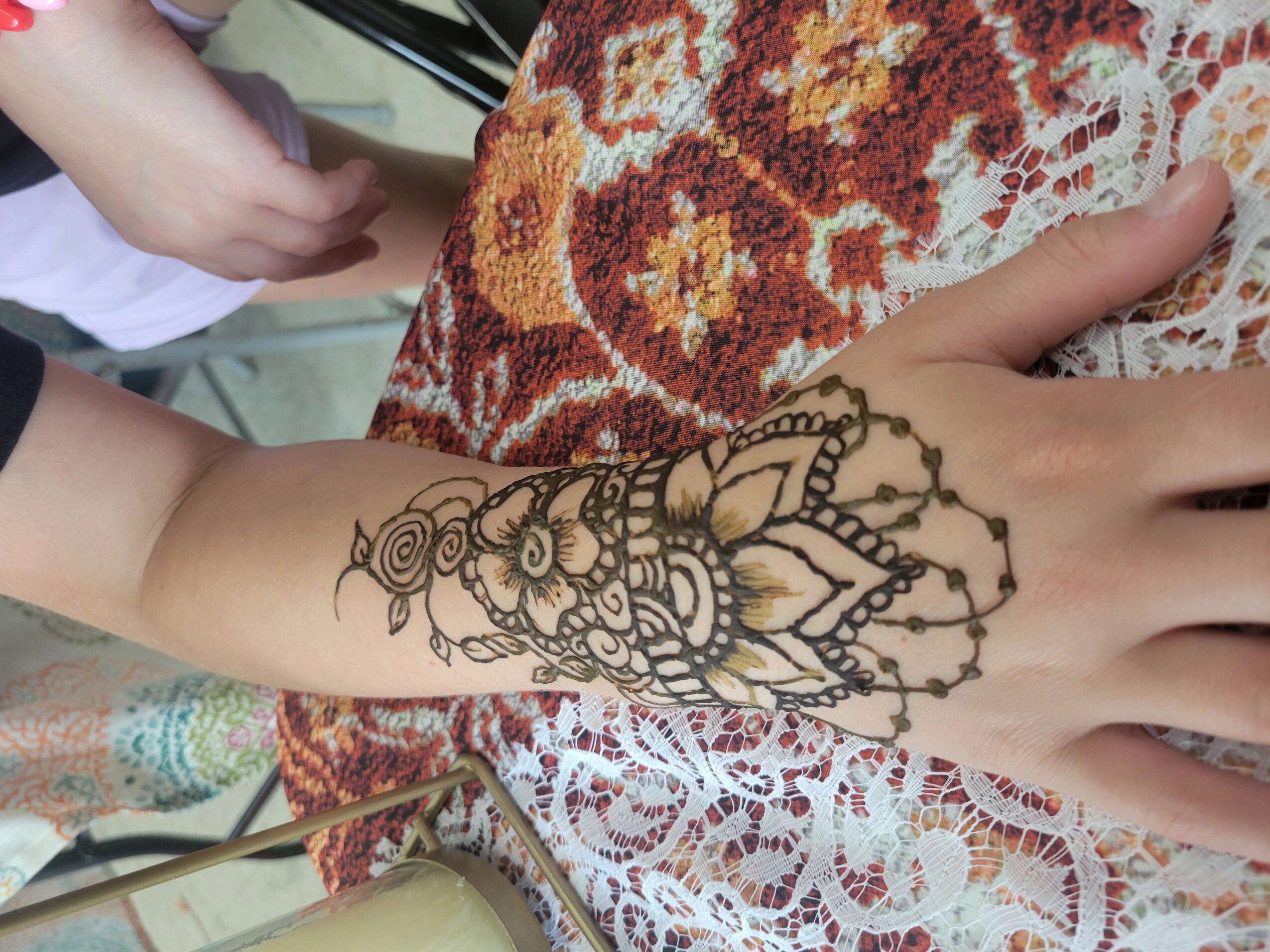 Child's hand with a detailed henna tattoo resting on a patterned fabric surface.