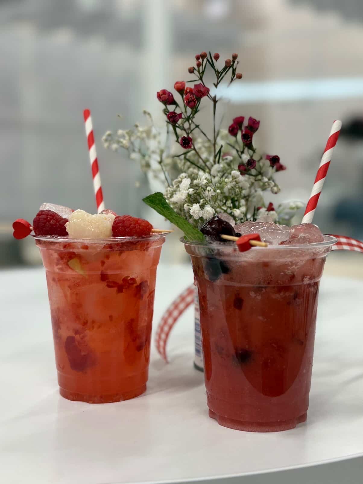 Two berry smoothies with striped straws, garnished with berries and flowers, on a white surface.