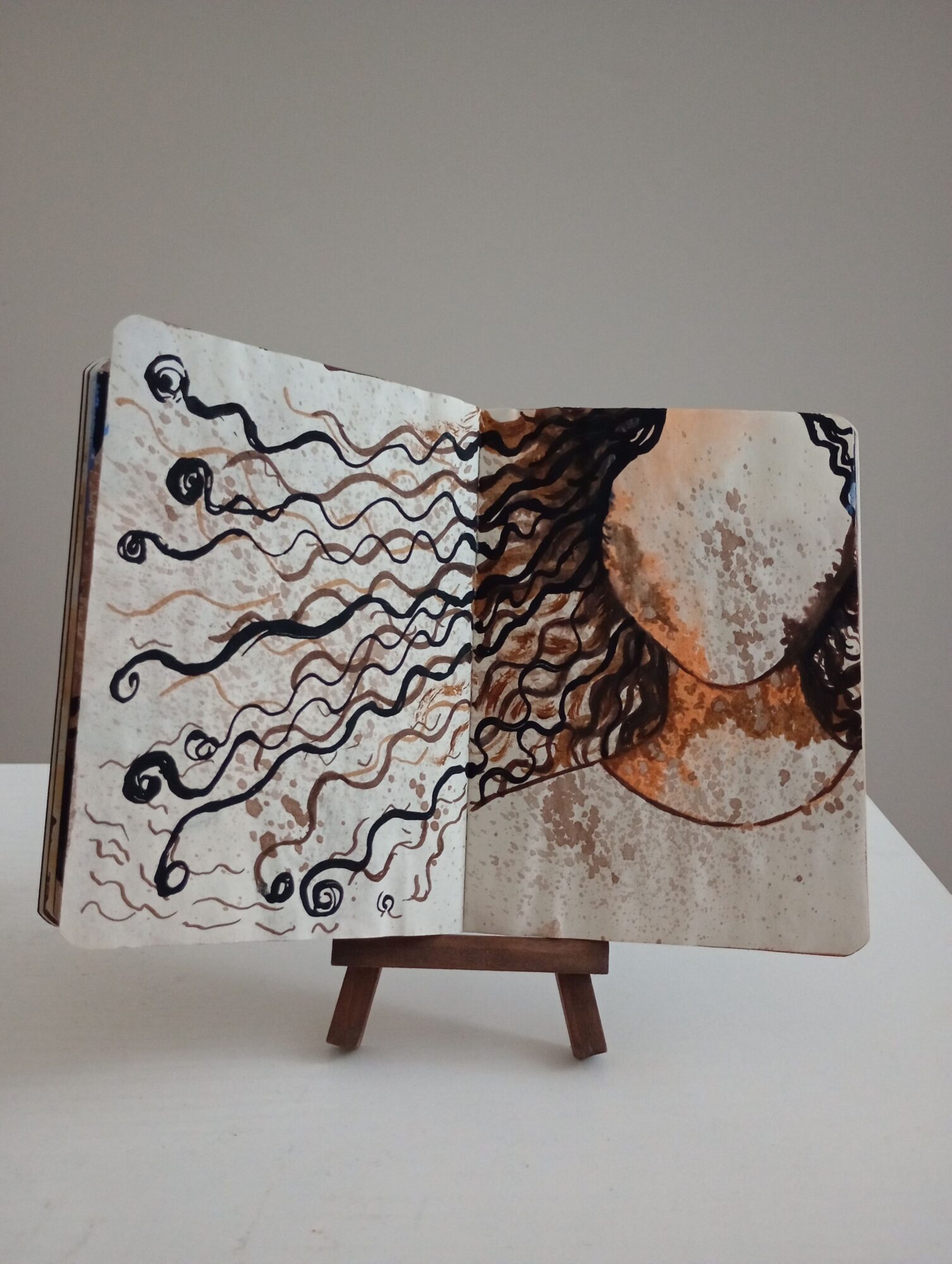 Book with an abstract cover design featuring curly lines and circular shapes, placed on a wooden stand against a plain background.
