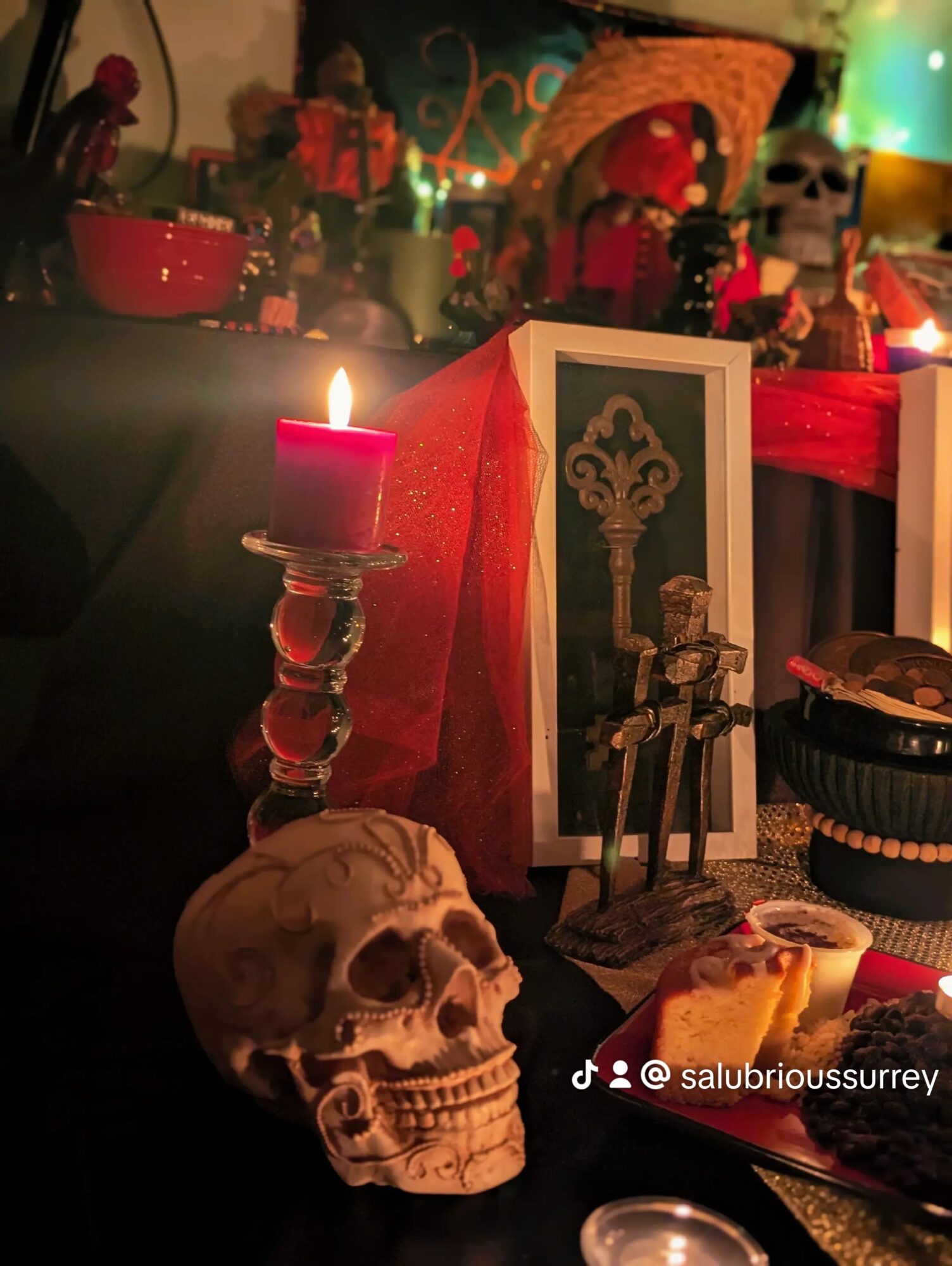 Decorative skull, lit candle, framed picture, and various objects on a table with colorful background lighting.