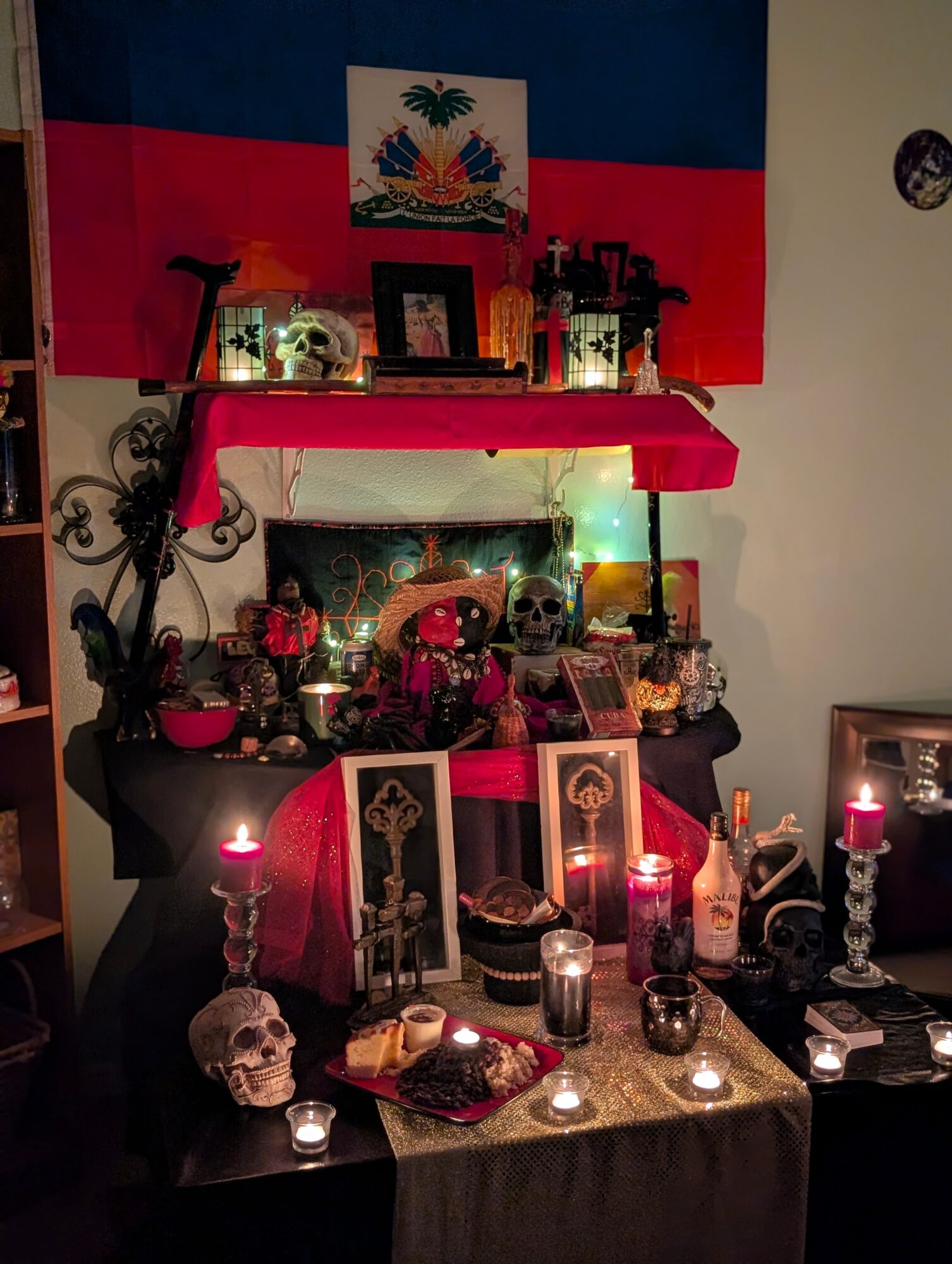 Day of the dead altar with skulls, candles, flowers, and photos, decorated with a flag in the background.