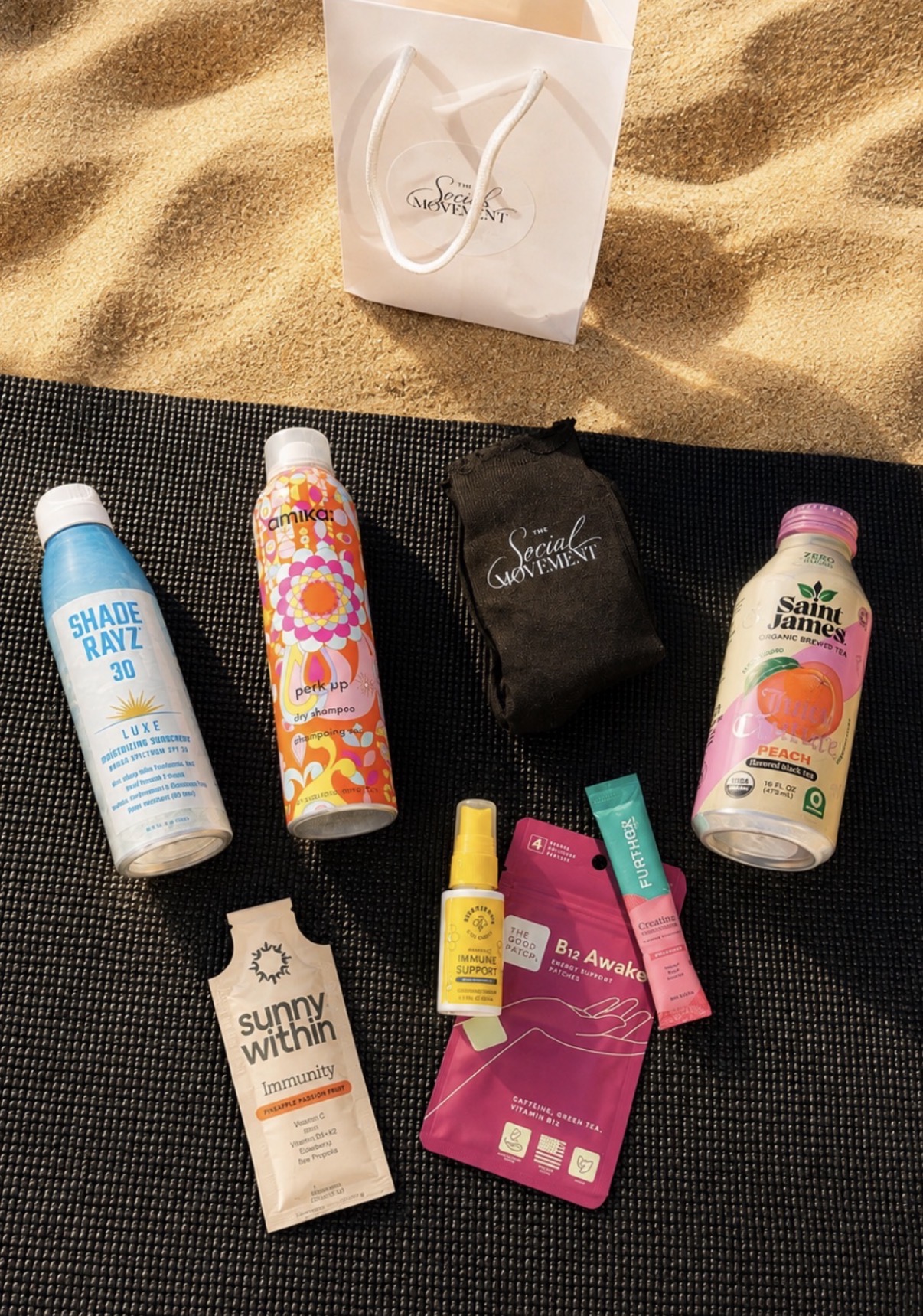 Sun protection products and a black pouch on a black mat, with a paper bag in the background on sand.