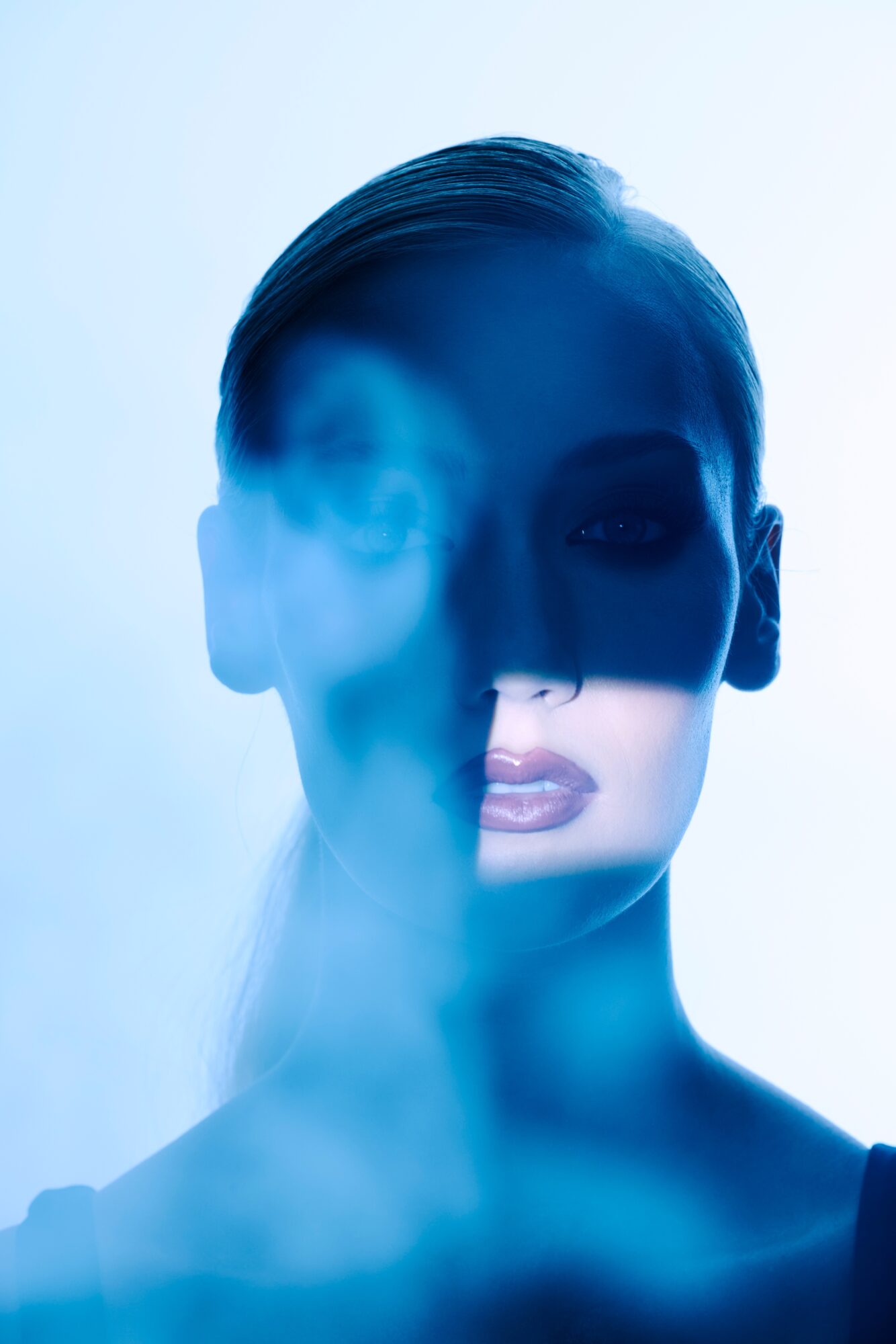 A woman with her face partially obscured by a shadow, with a blue tint and a misty effect.