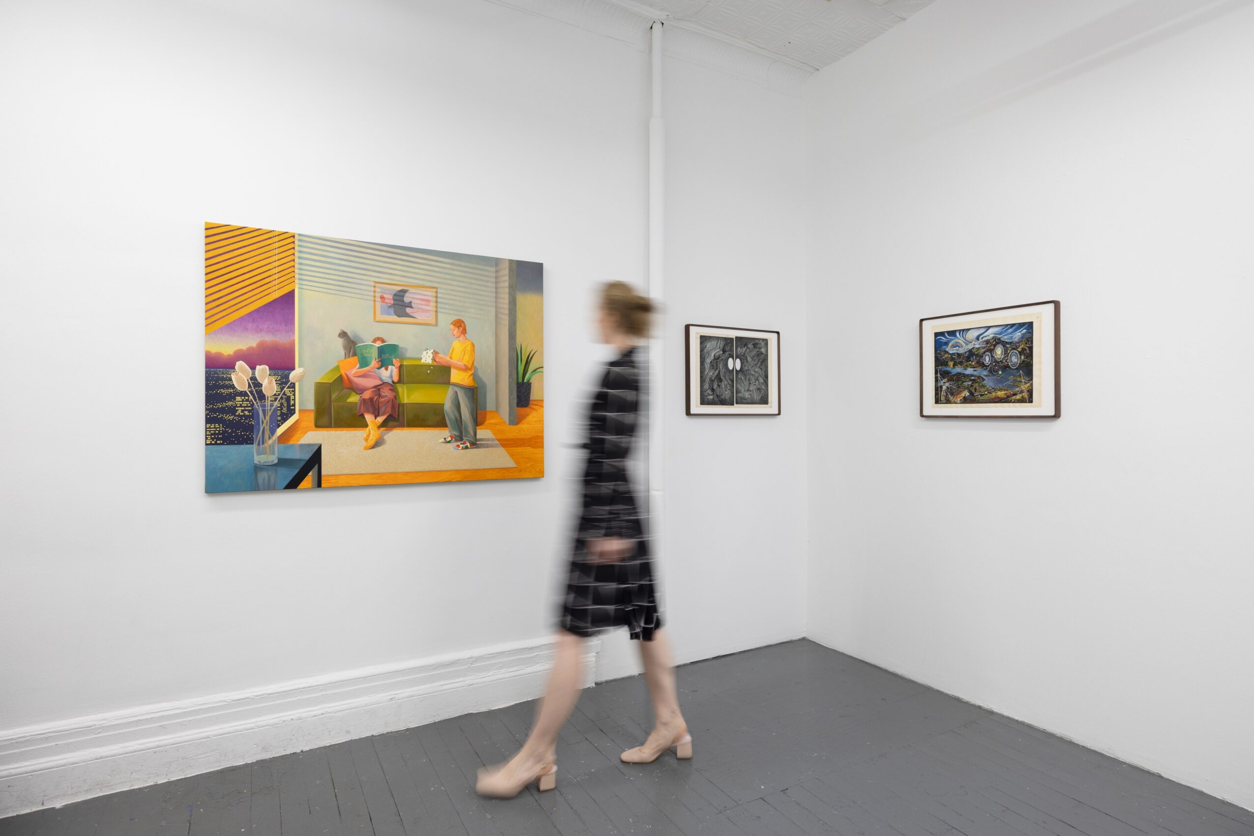 A person walks through a white-walled gallery displaying three framed artworks.