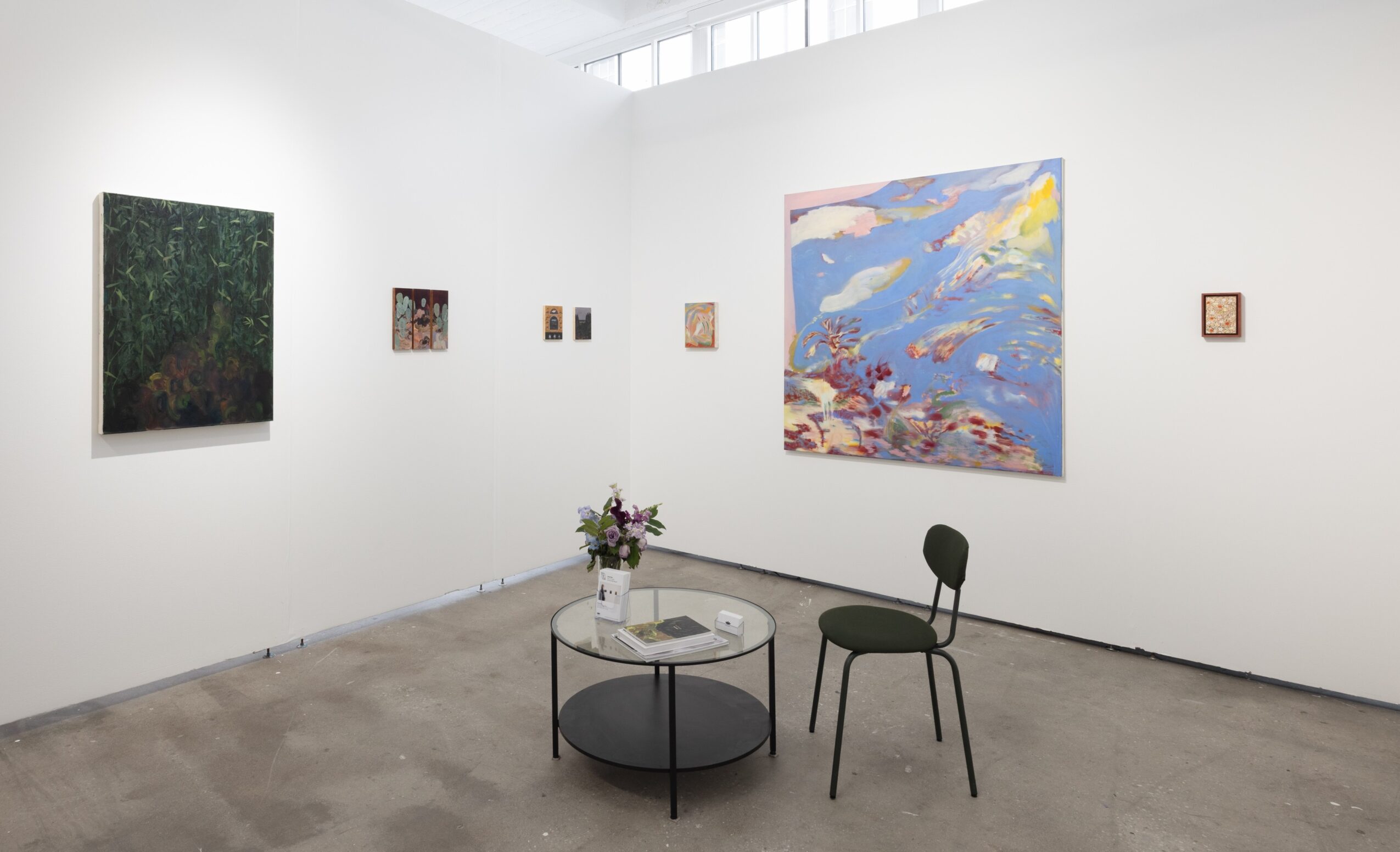 Bright gallery with several paintings, a small round table with flowers, and two chairs.