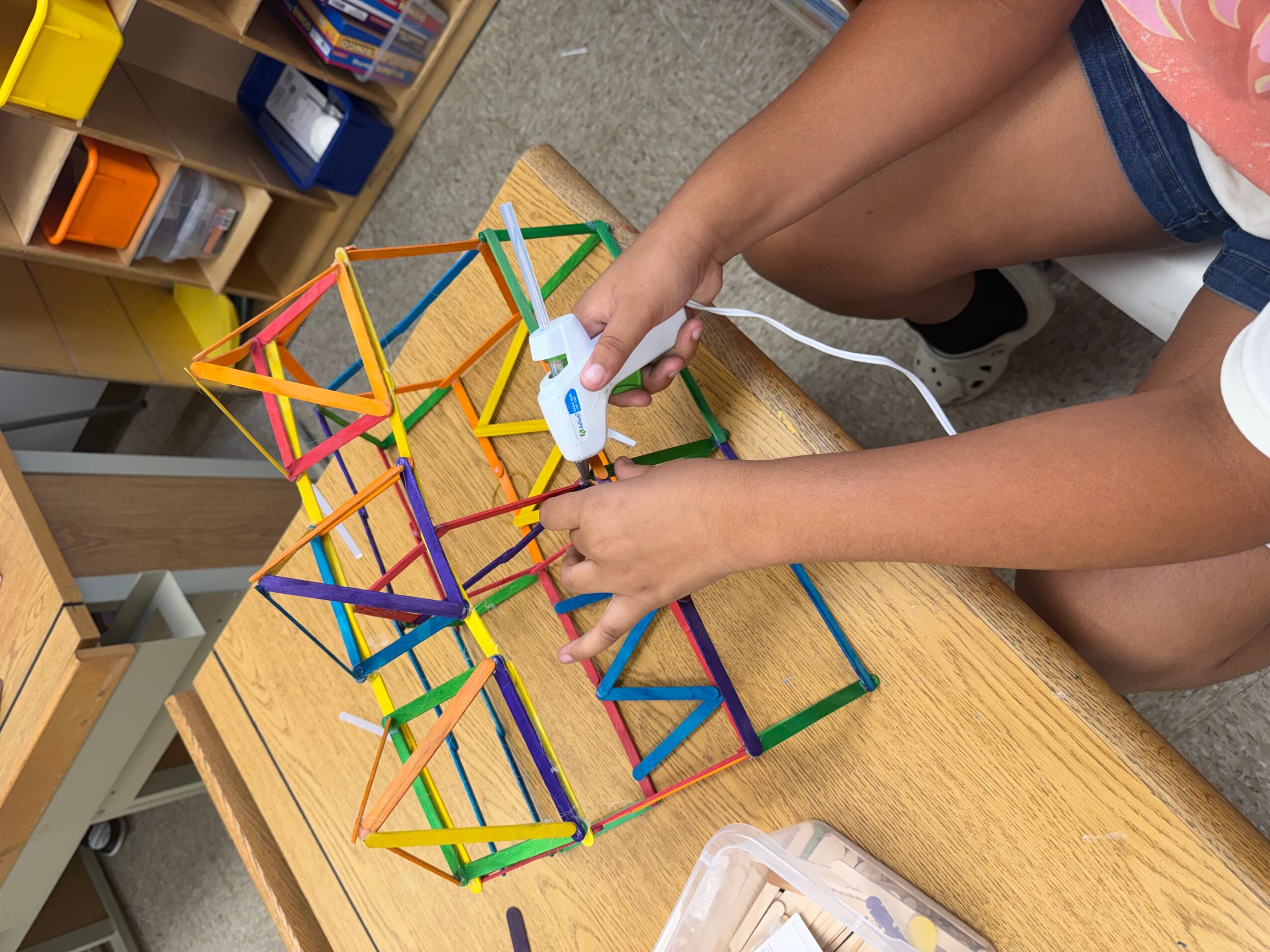Person uses a handheld controller beside a colorful geometric construction on a wooden table.