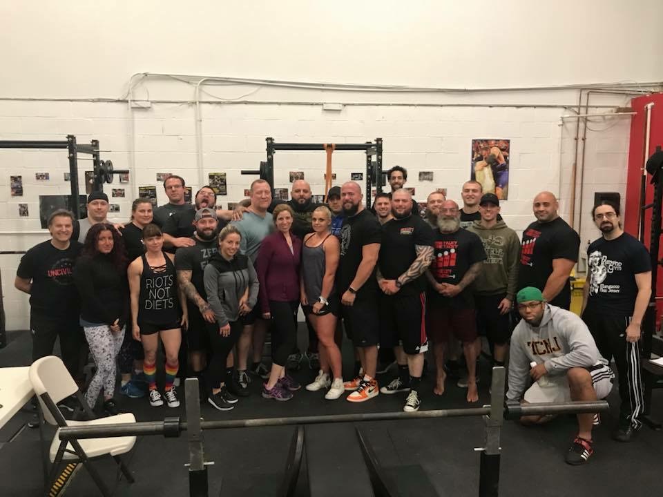 Group of people posing around weightlifting equipment in a gym.
