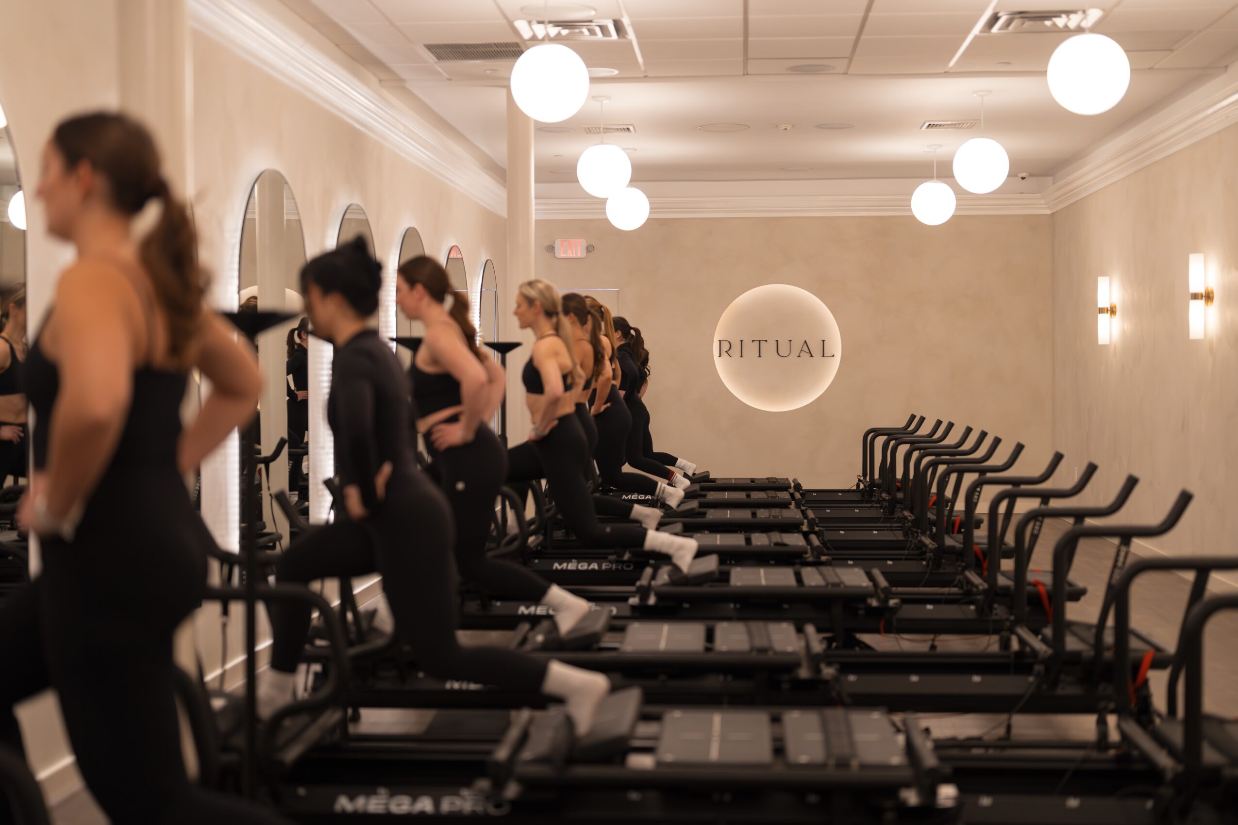 People using treadmills in a fitness studio with a sign reading 'RITUAL' on the wall.