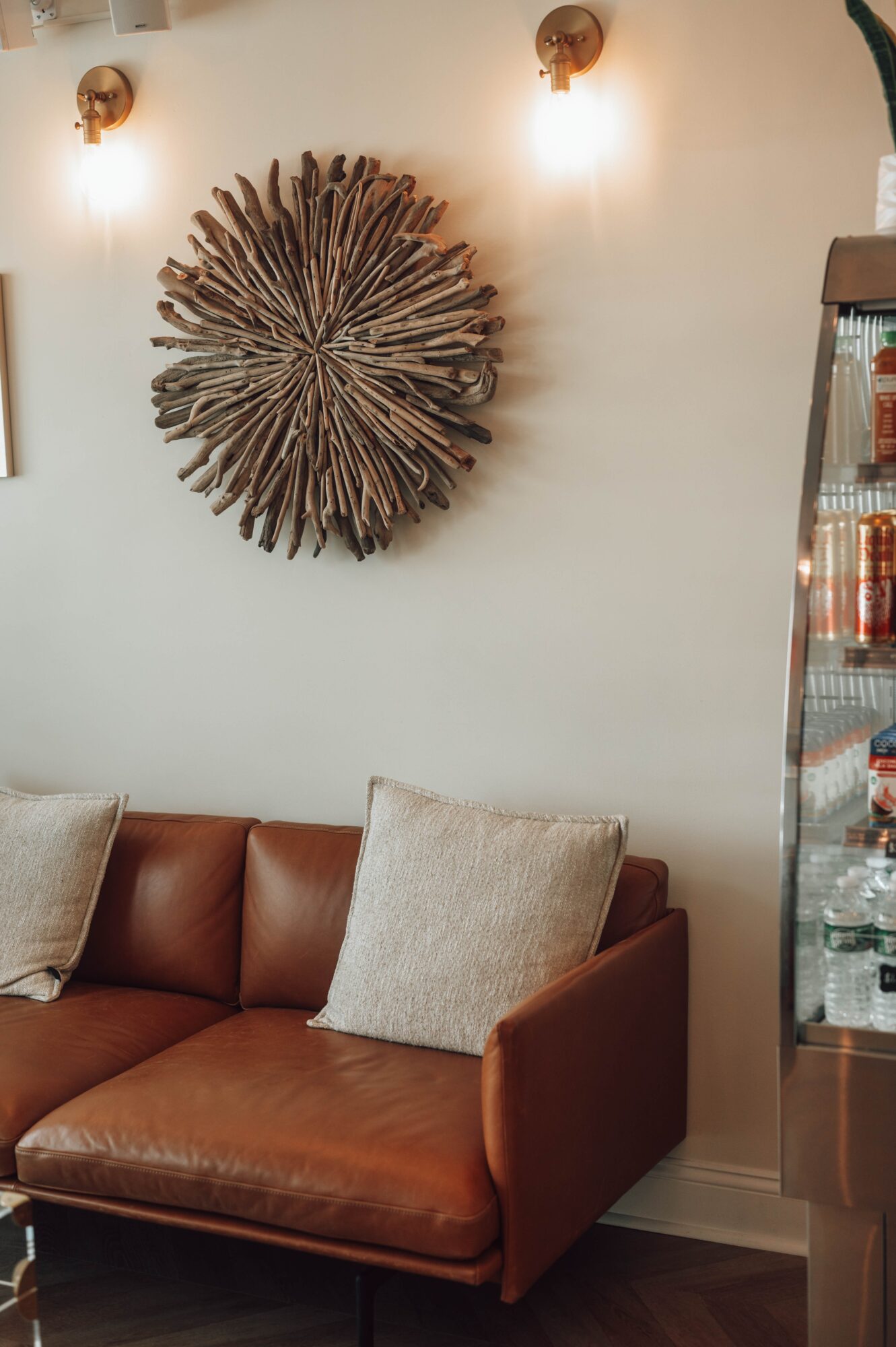 Living room corner with a brown leather sofa, beige cushions, wall art, and a glass display cabinet.
