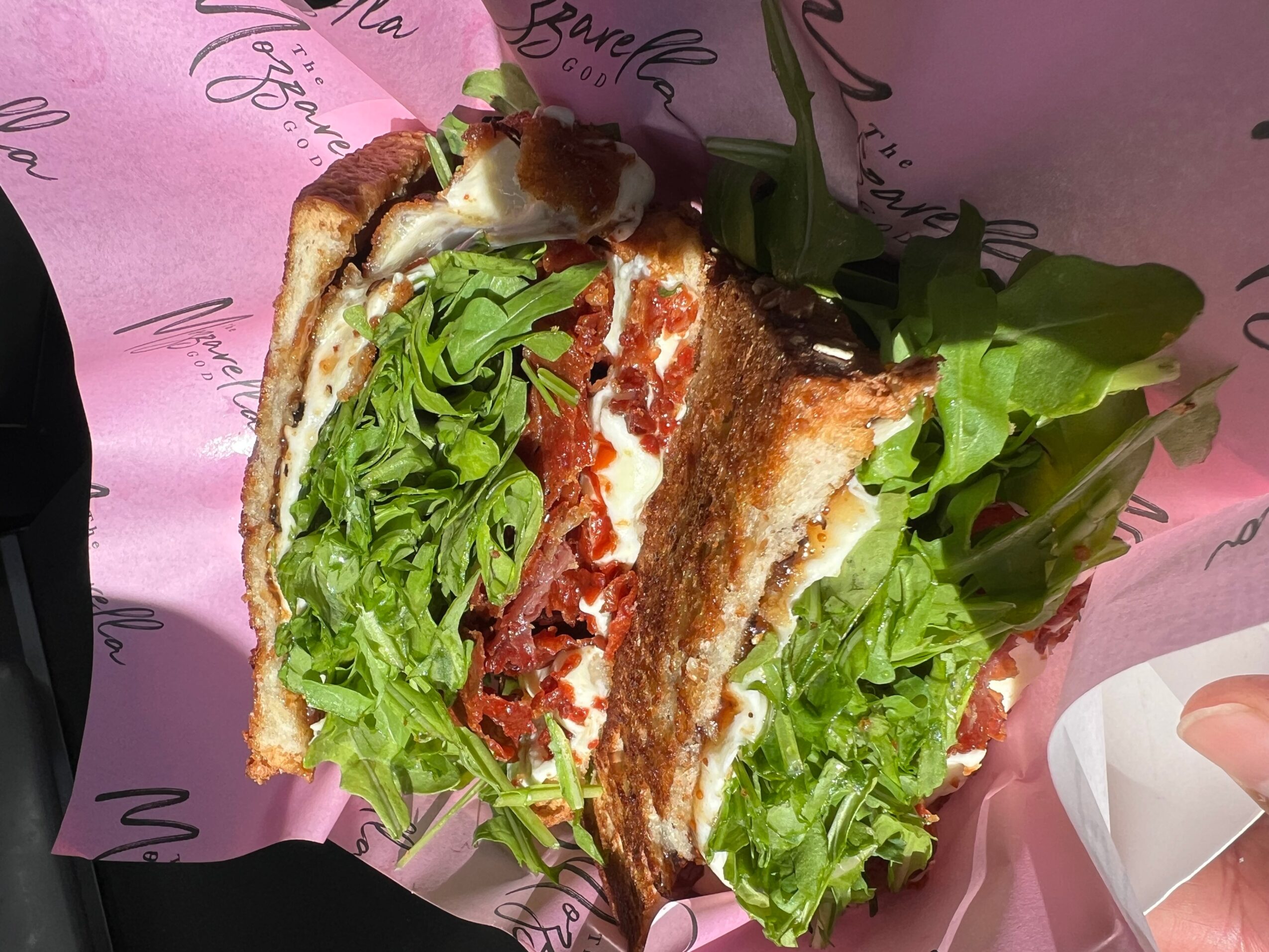 Sandwich with lettuce, tomato, and toasted bread, wrapped in pink paper with black writing
