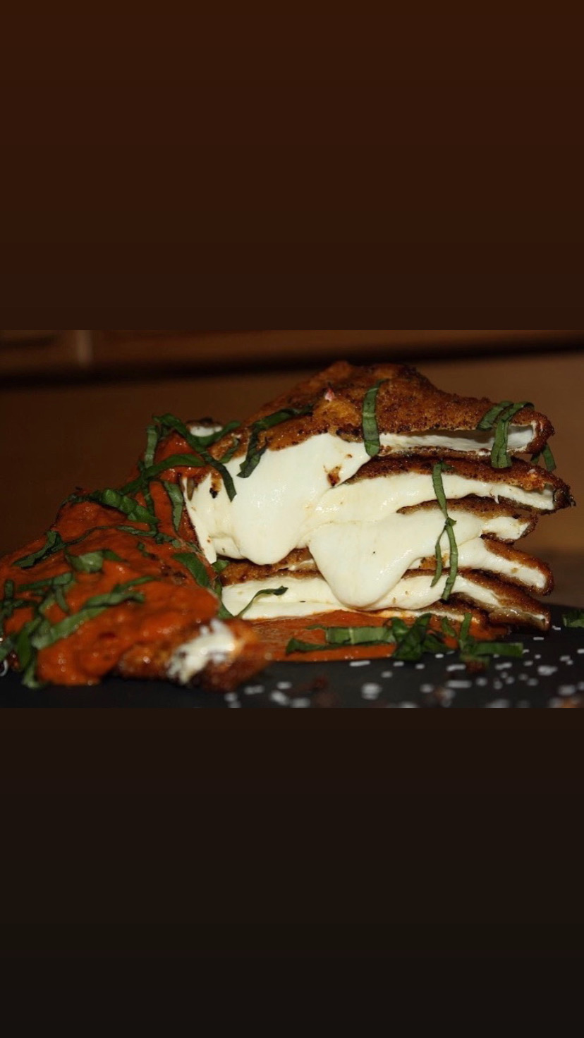 Stacked waffles topped with whipped cream, chocolate sauce, and garnished with green herbs, on a dark surface.
