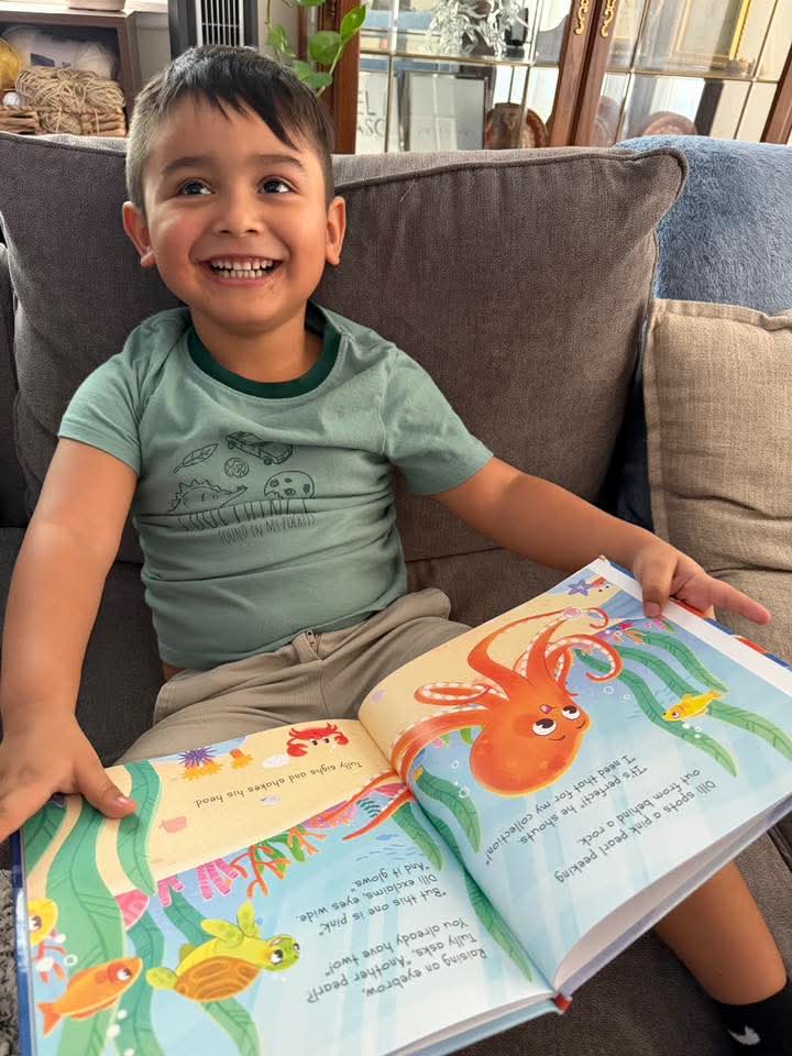 Child smiling and sitting on a couch, holding an open colorful children's book with an octopus illustration.