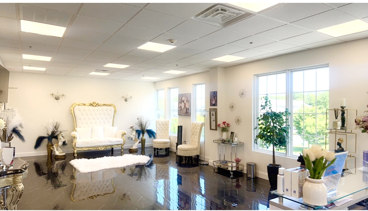 Elegant room with a high-backed white sofa, chairs, large windows, and decorative plants, bright and spacious.