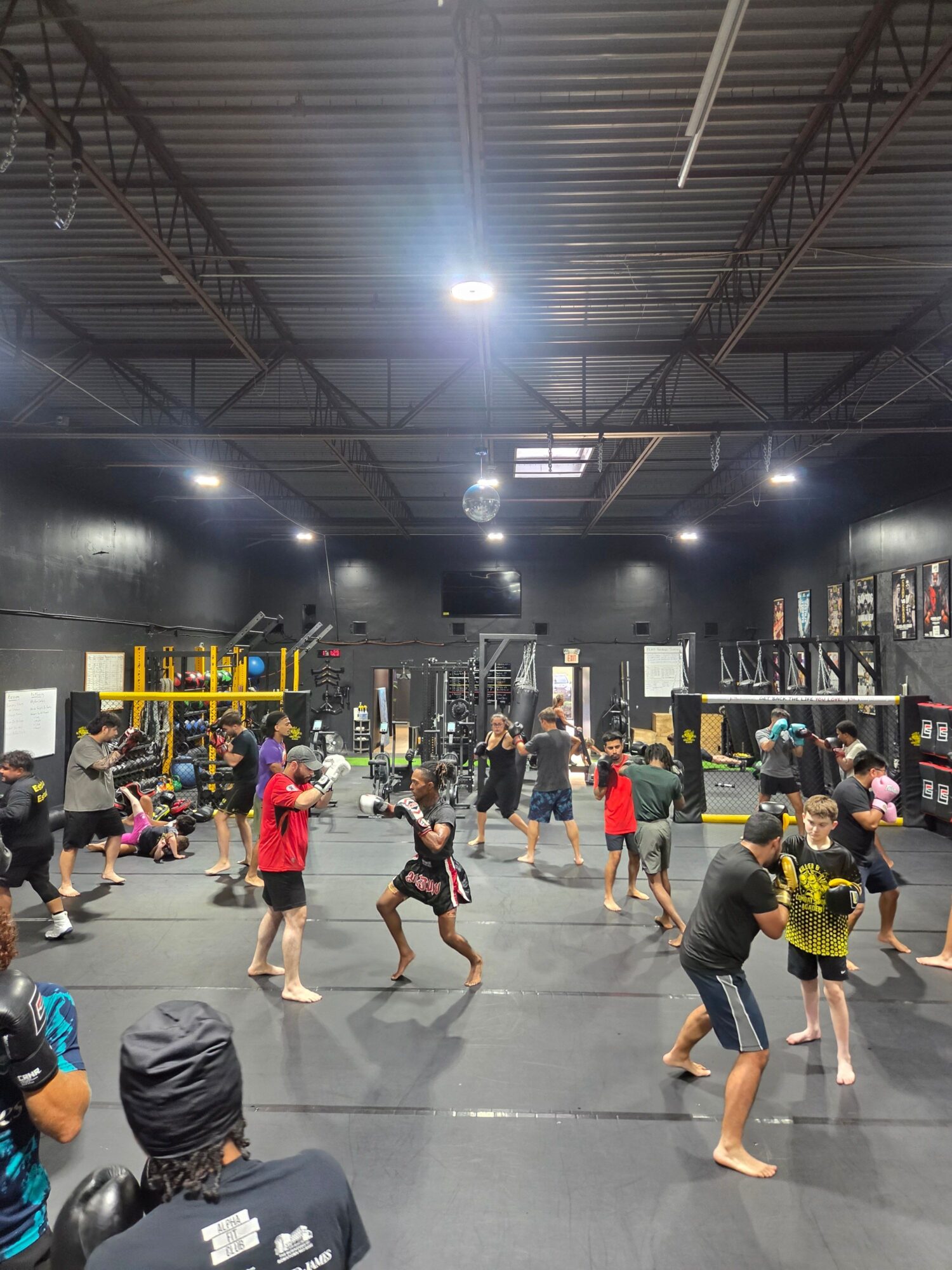 People practicing dance or fitness in a spacious indoor gym with equipment and bright lighting.