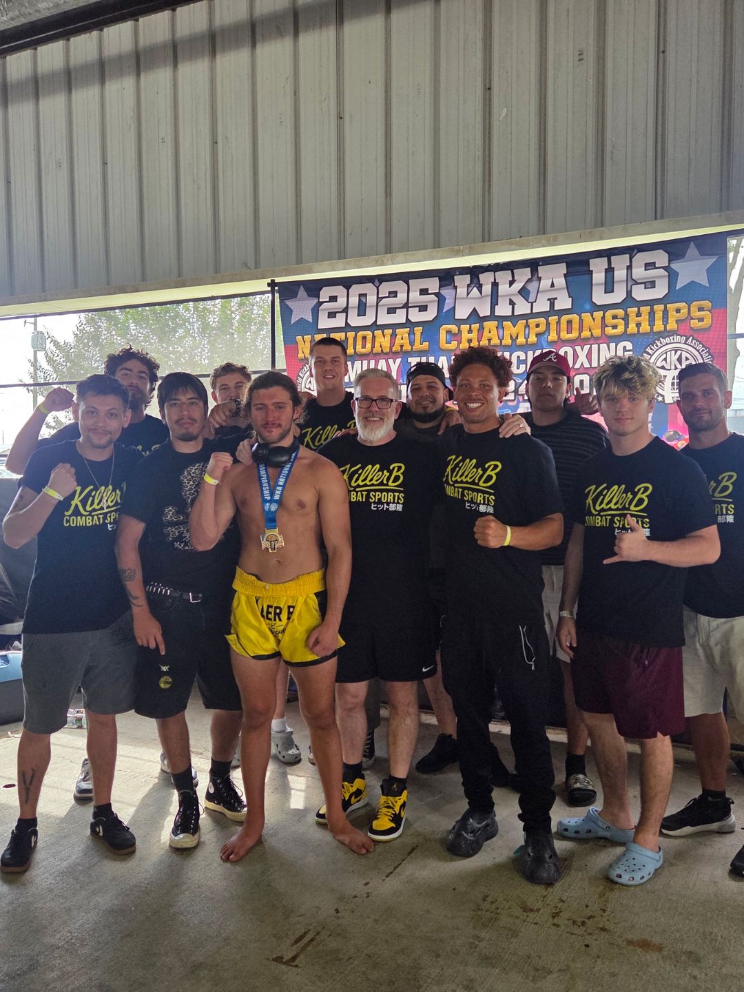 Group of people, some with medals, standing in front of a banner at a sports event, smiling and posing for the photo.