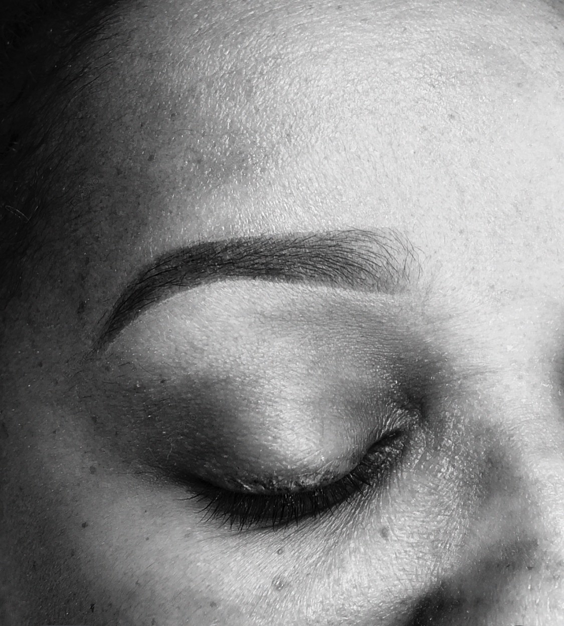 Close-up of a person's closed eye, eyebrow, and part of the forehead in black and white.