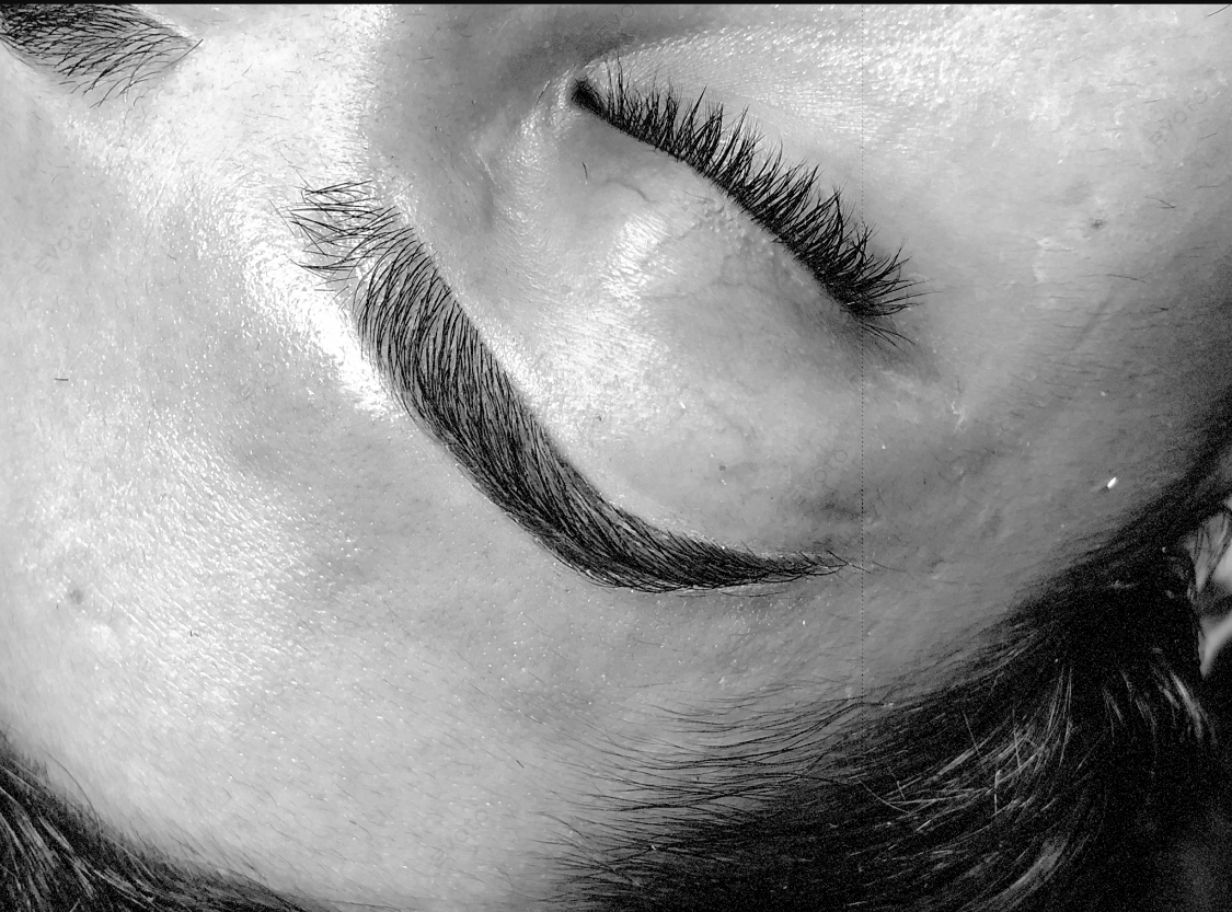 Close-up of a person's closed eye, eyebrow, and eyelashes in black and white.