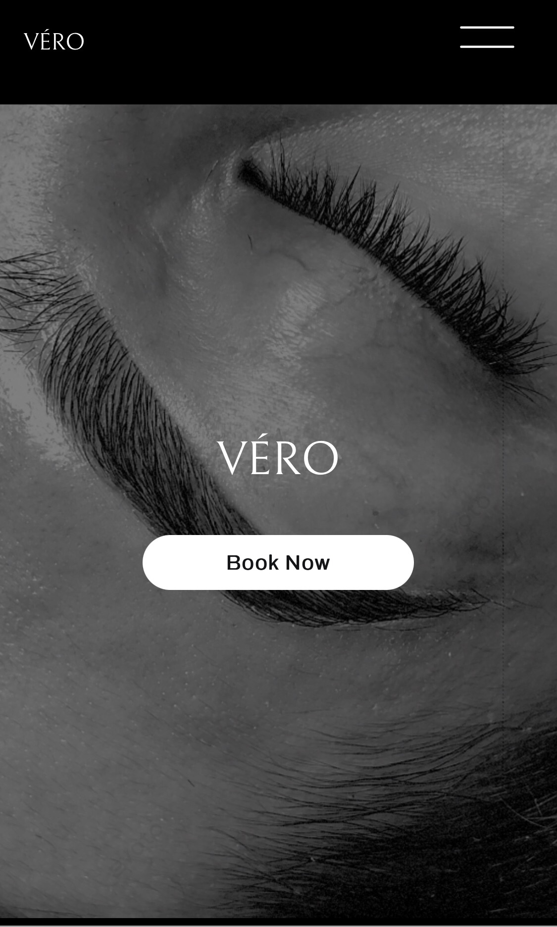 Close-up of a person's eye with long eyelashes, eyebrow, and skin texture in black and white.