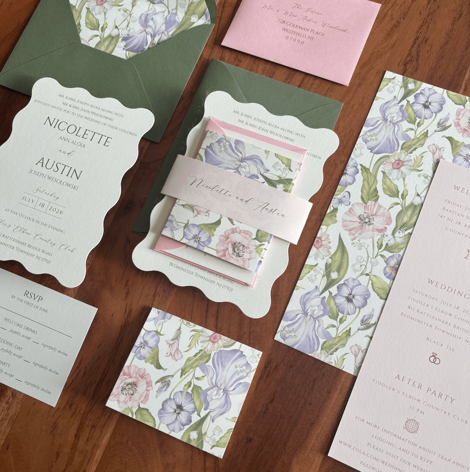 Wedding invitation suite with floral design, RSVP card, and pink note on wooden surface.