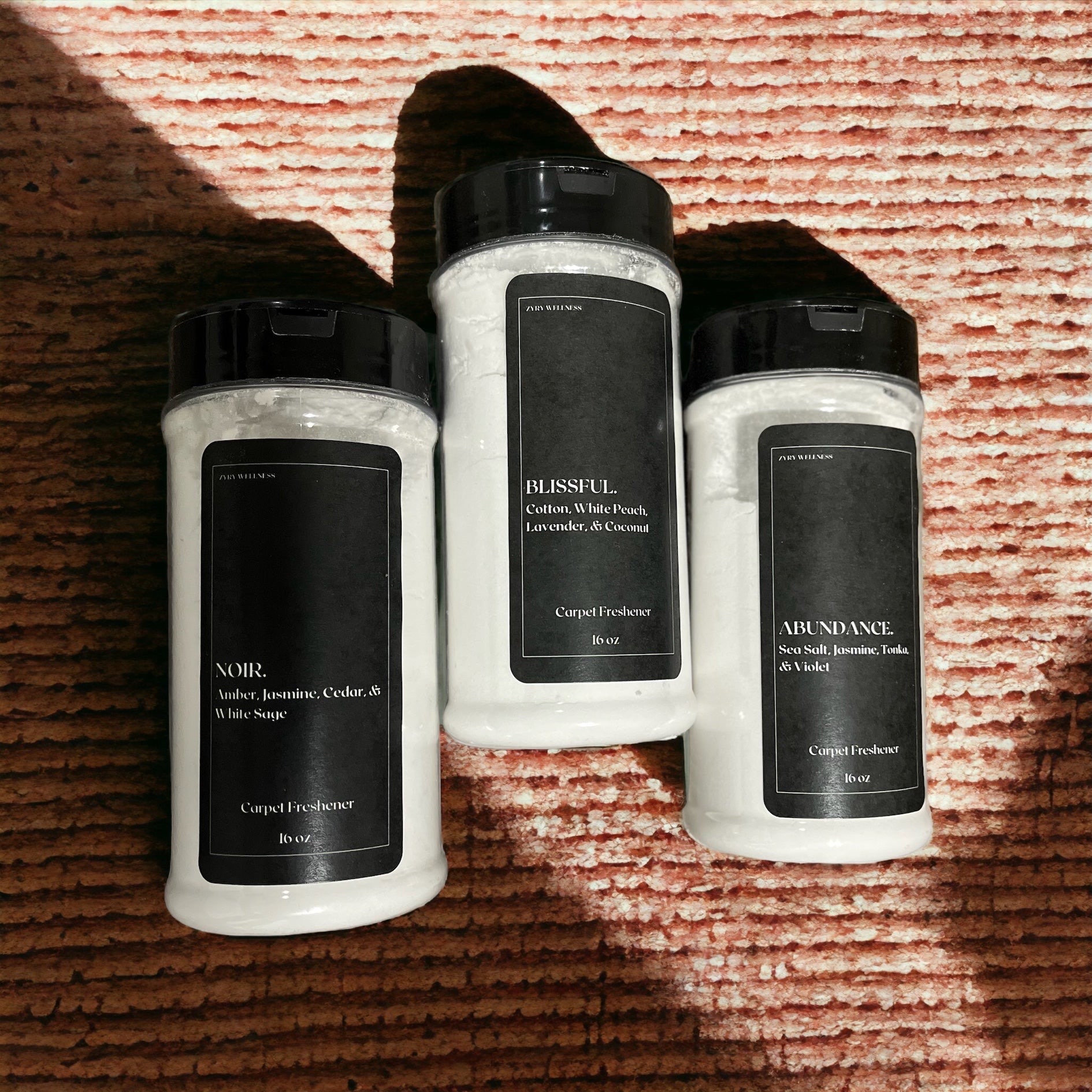 Three bottles of carpet freshener on a textured surface with shadows, black labels, and white bottles.