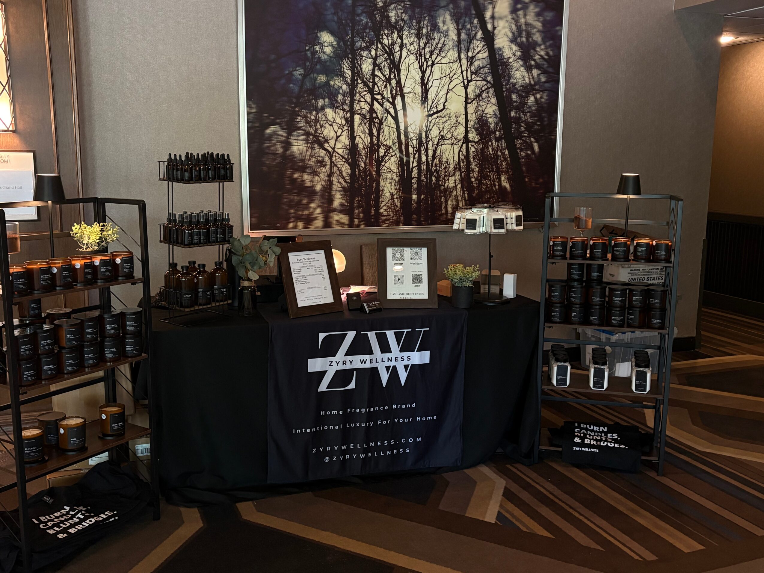 Display table with skincare products, framed pictures, and a banner, set against a large forest picture on the wall.