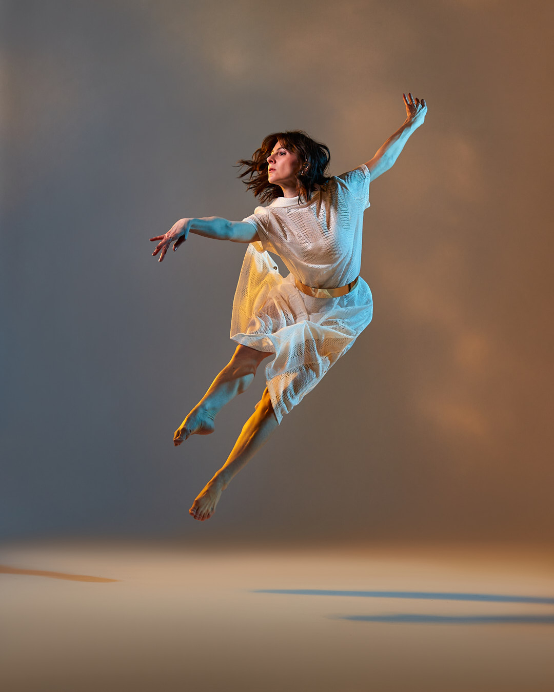 A woman in a flowing dress jumps in the air with arms outstretched against a gradient background.